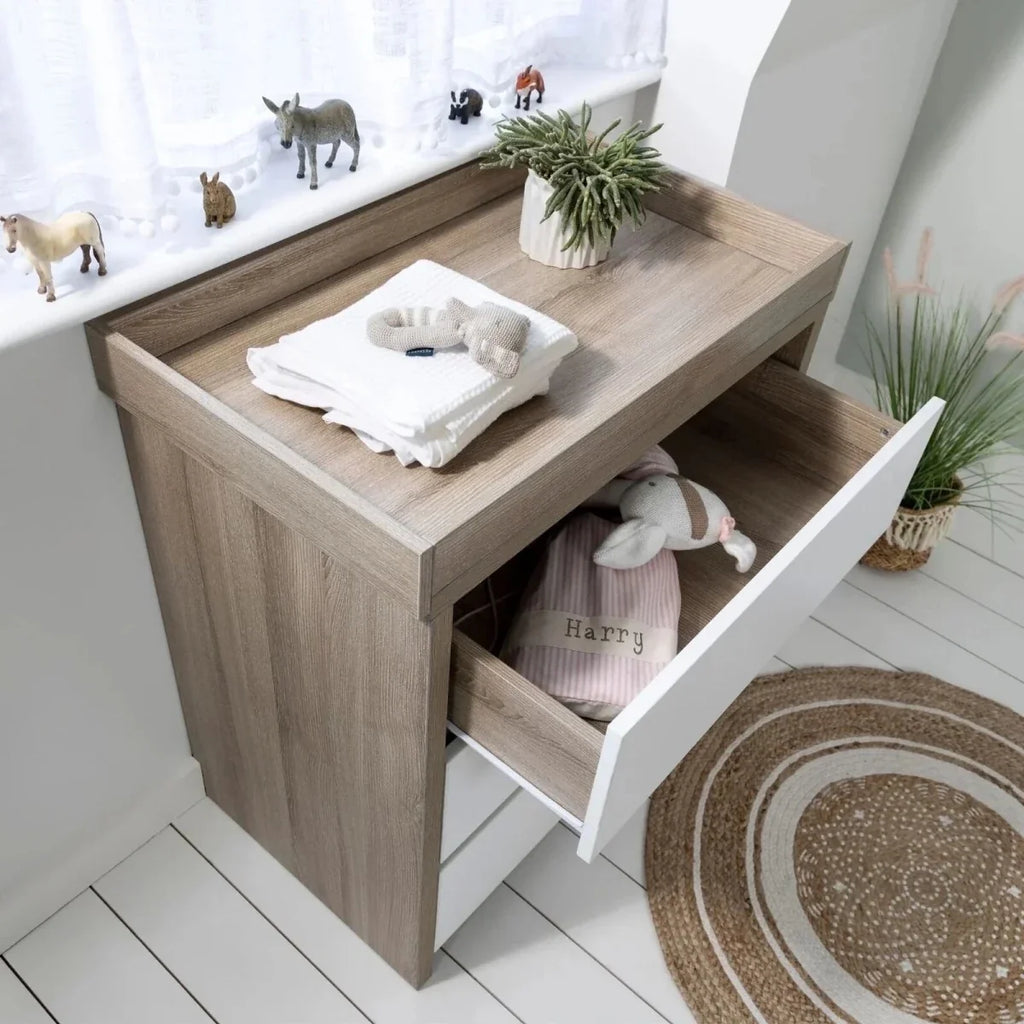 Oak cot bed with built-in drawer underneath and folded bedding inside drawer