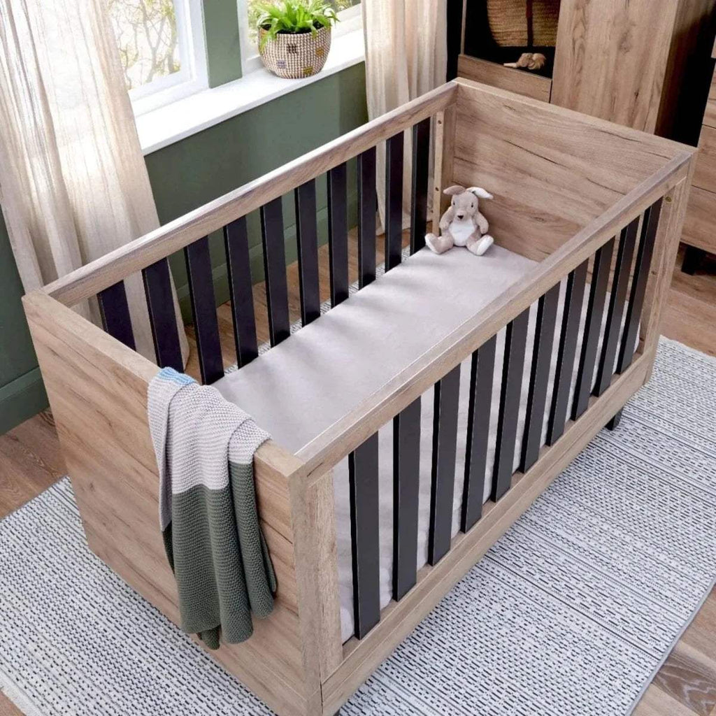 Distressed oak cot bed with slate-grey slat rails and white mattress bedding.