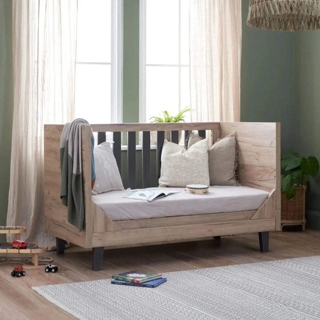 Distressed oak cot bed with slate-grey slat sides and layered white pillows.