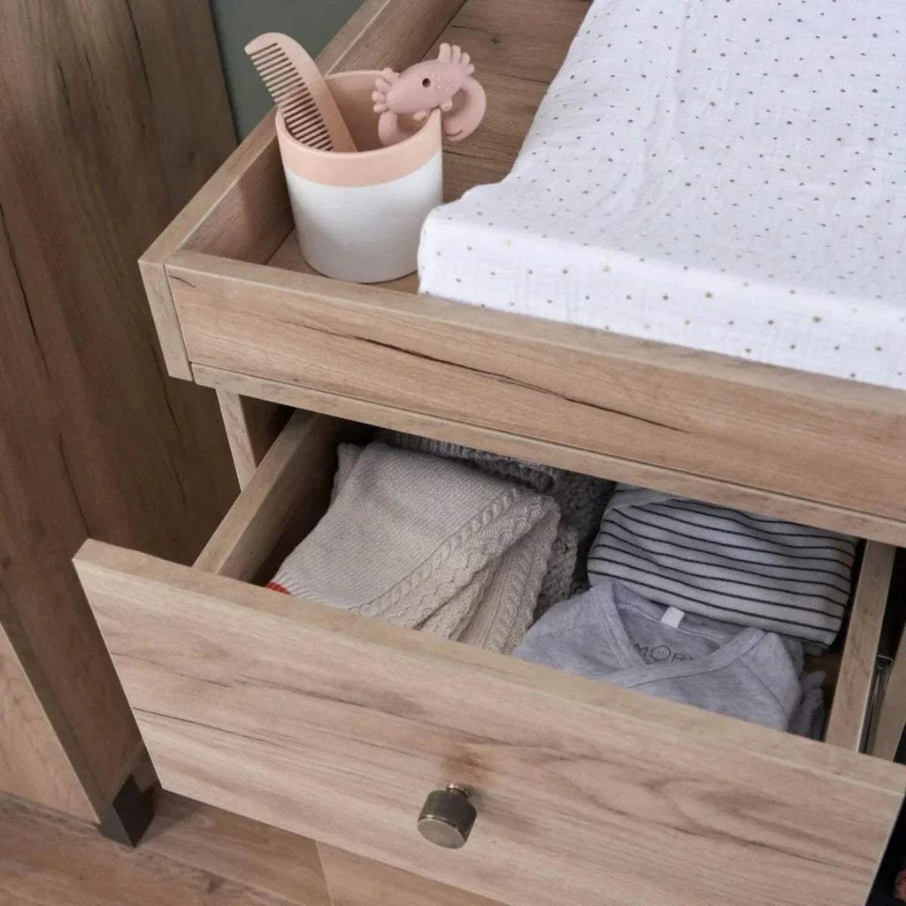 Distressed oak bed frame with open storage drawer and folded linens inside.