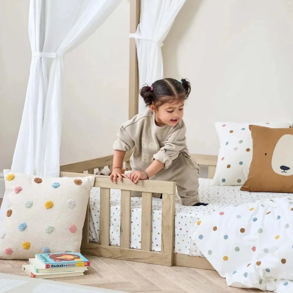 Oak toddler floor bed with low rails and dotted bedding, toddler playing on mattress