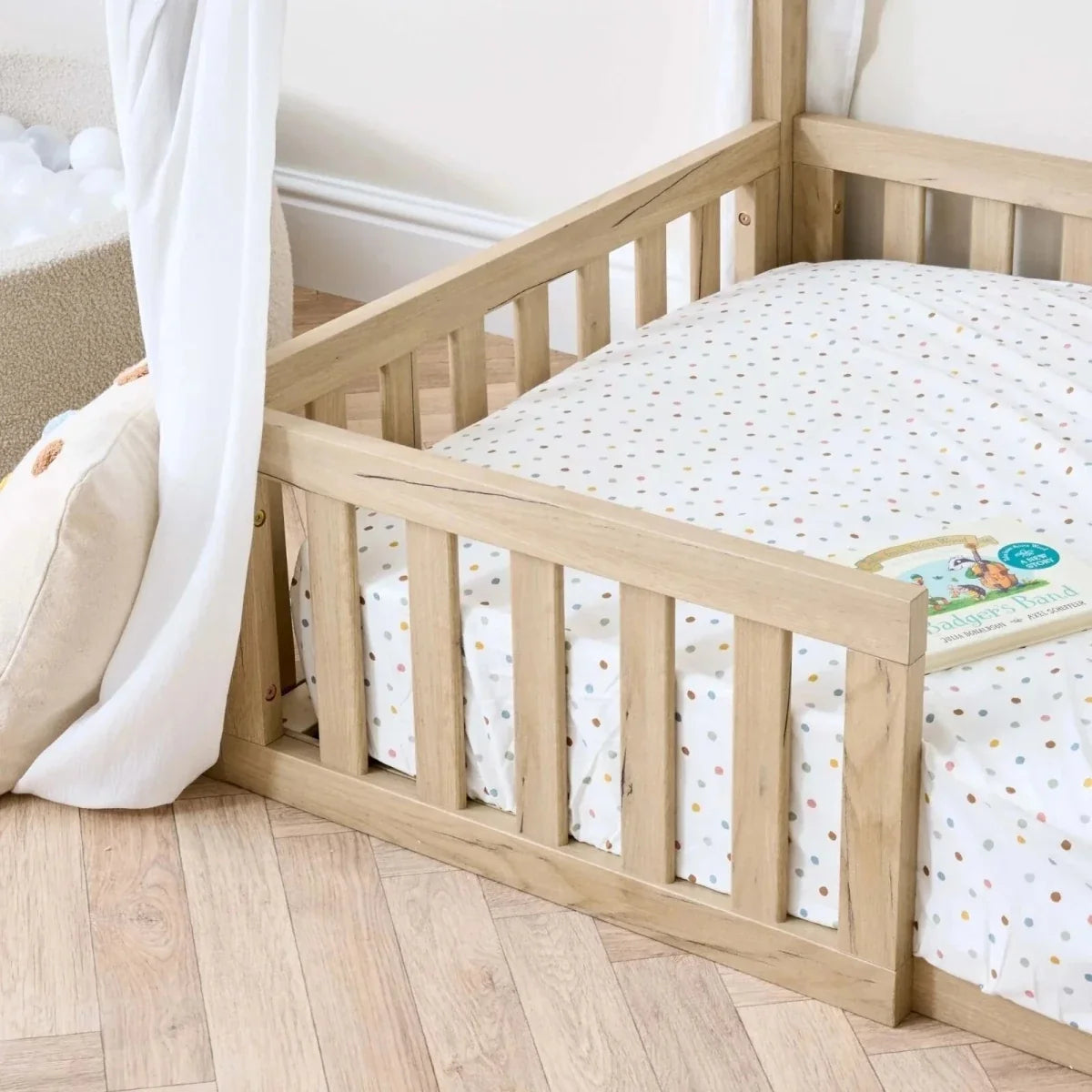 Oak toddler floor bed with low guard rail, dotted bedding, and white canopy curtains