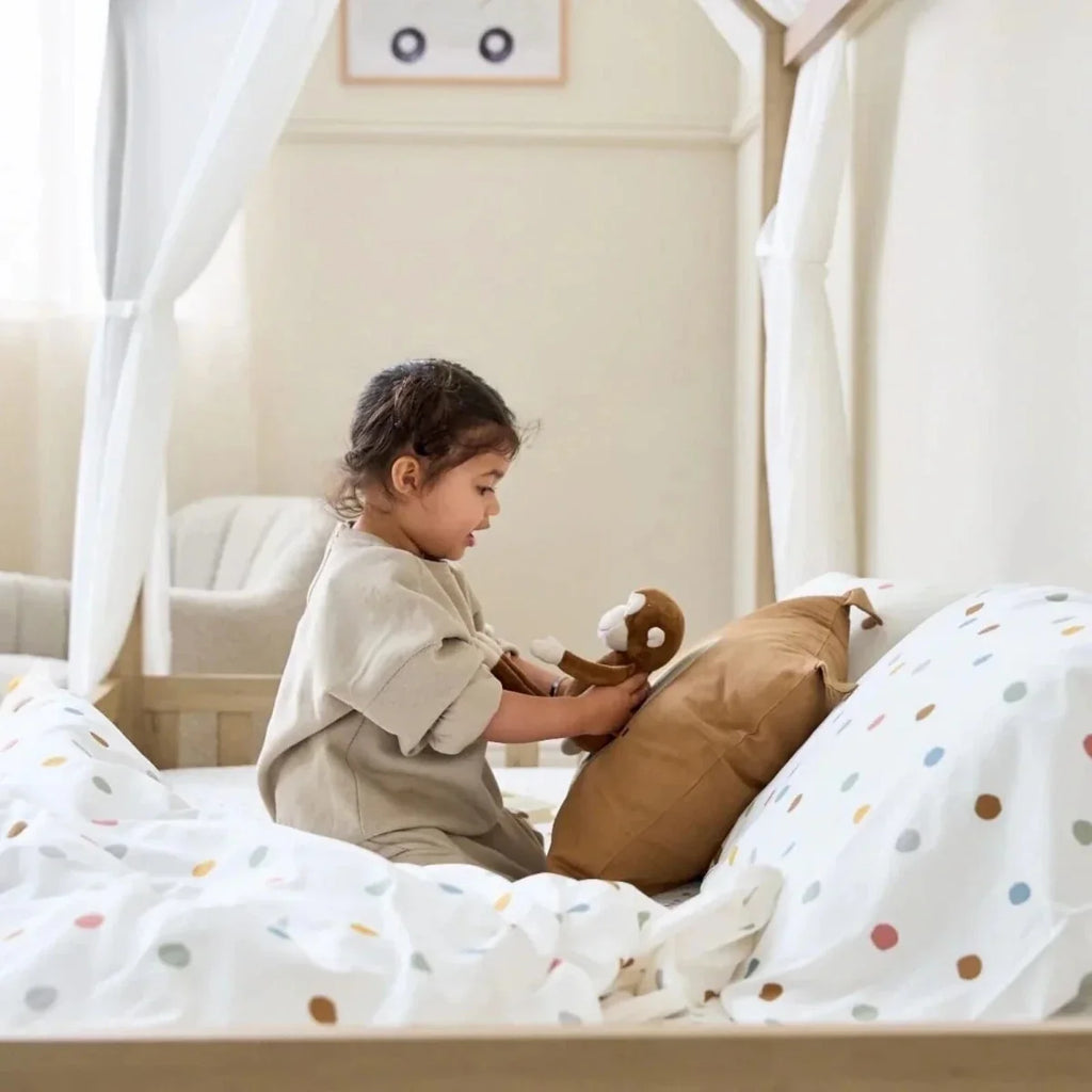Oak toddler floor bed with low rail, dotted bedding, and child reaching across pillows