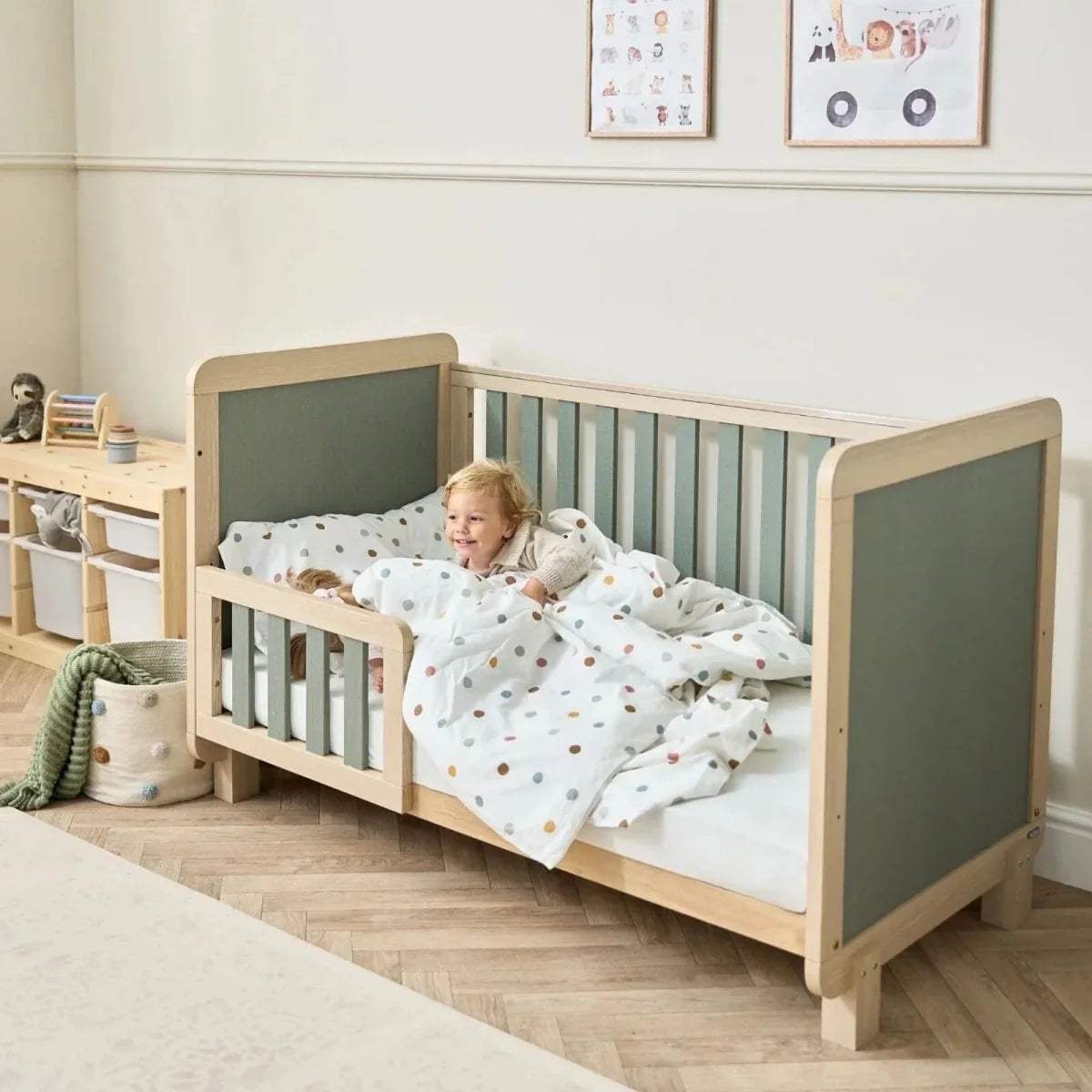 Wooden cot bed with sage panels and vertical slats, with child bedding