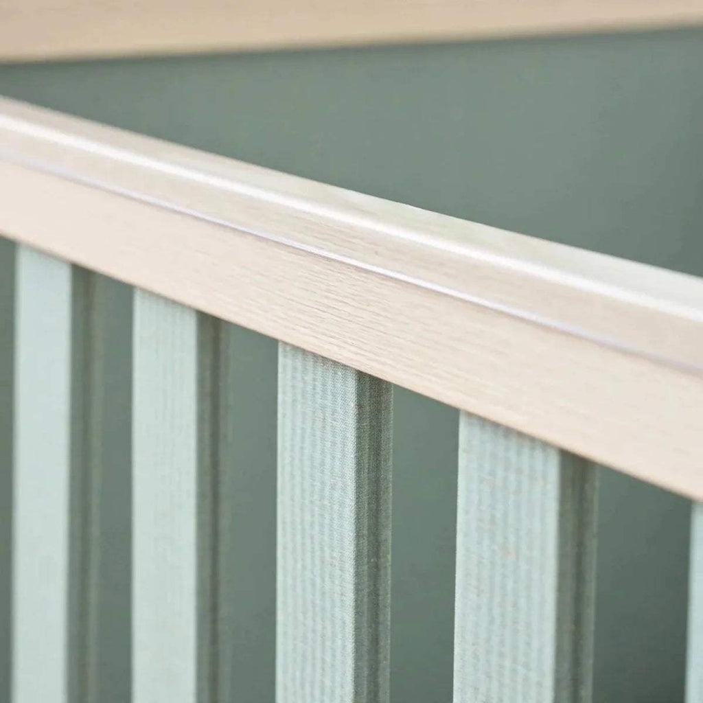 Close-up of golden oak cot bed slats with sage panel backing
