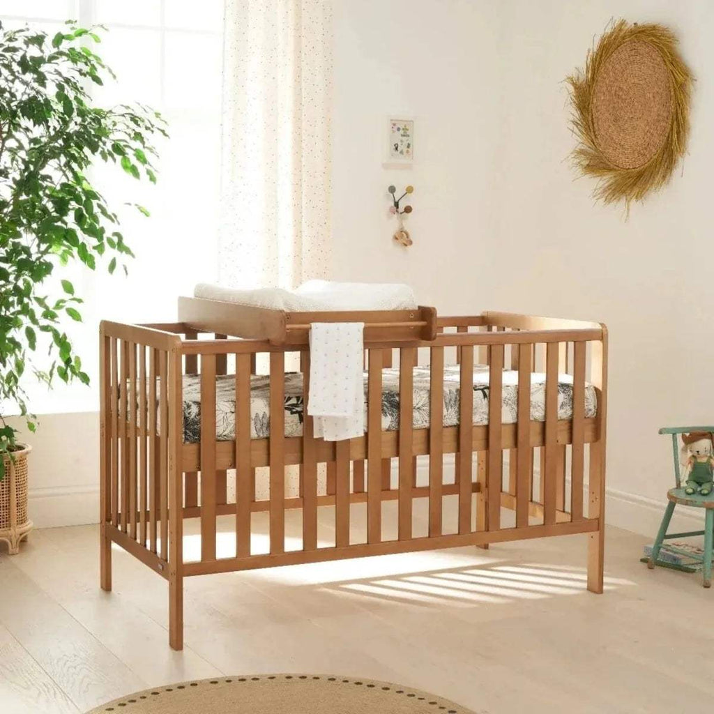 Wooden cot bed with vertical slat rails and cot top changing pad