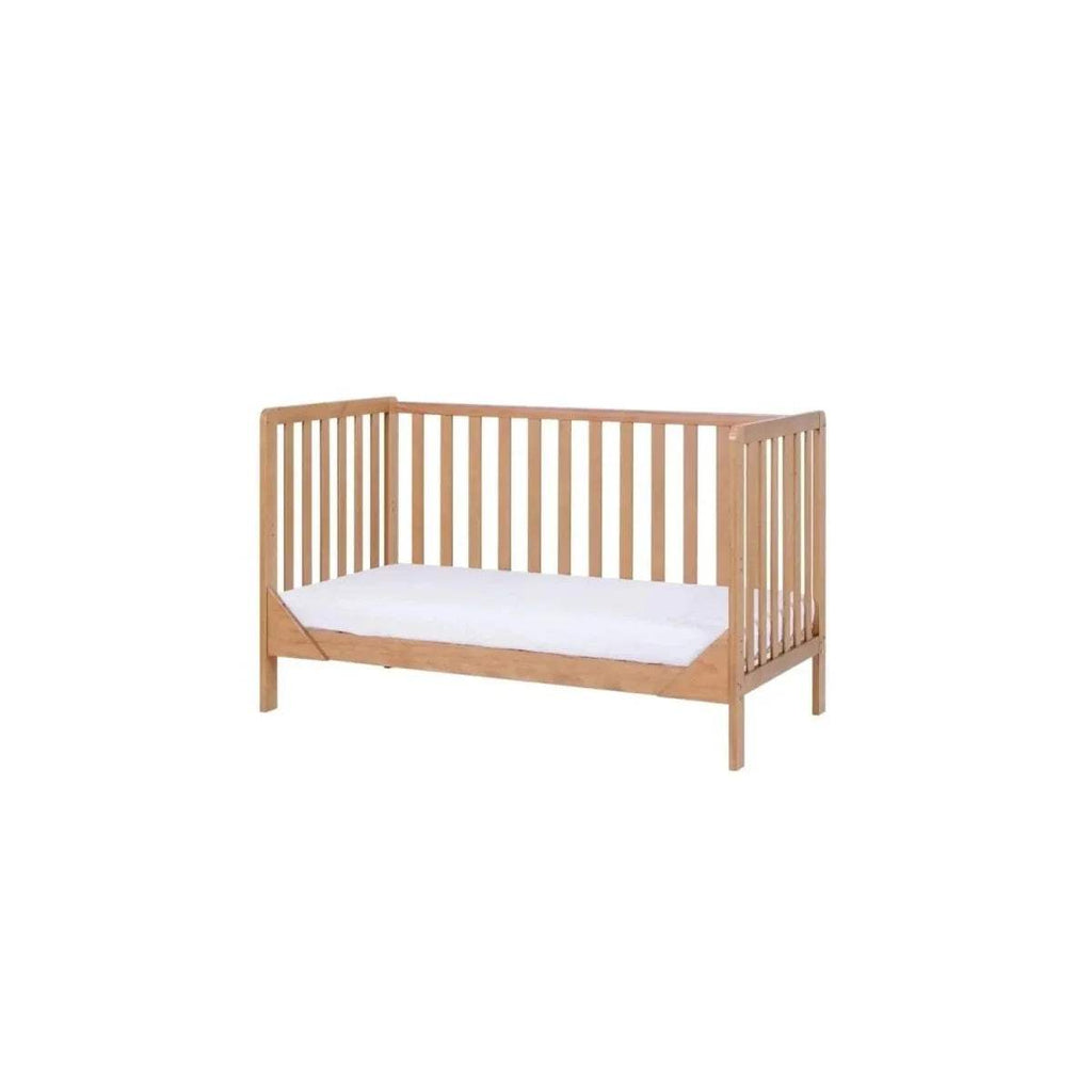 Wooden cot bed with vertical slat rails and white mattress pad