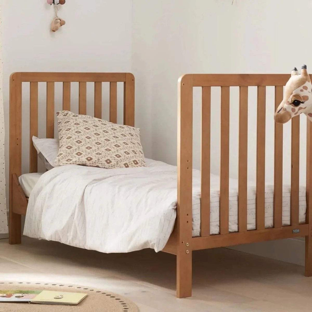 Wooden cot bed with white bedding and patterned pillow, side view