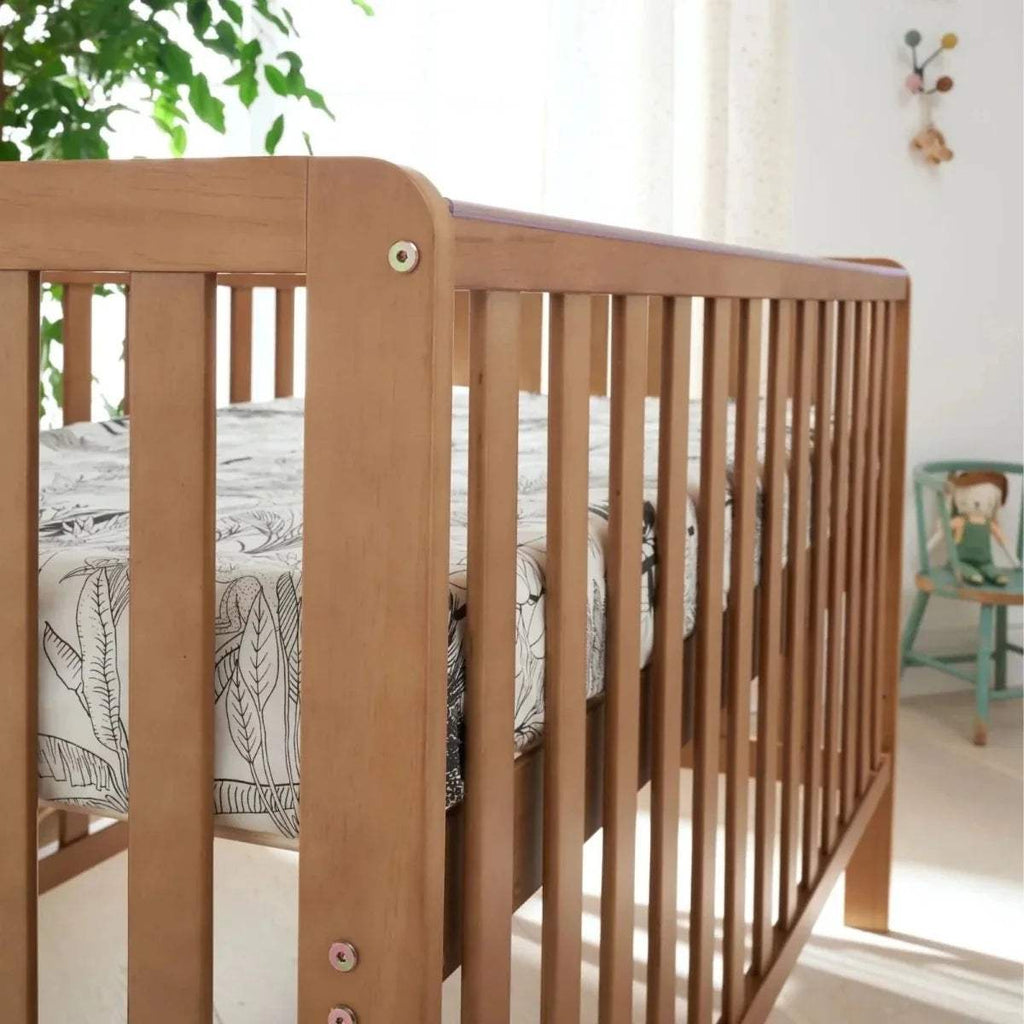 Wooden cot bed corner with vertical slats and round detail bolts, close-up