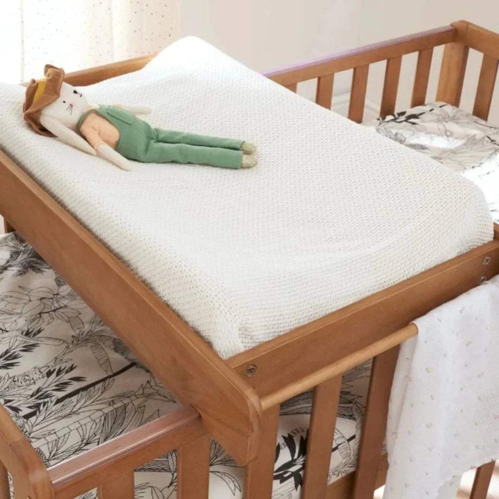 Wooden cot bed with white mattress, textured blanket, and slatted head and foot rails