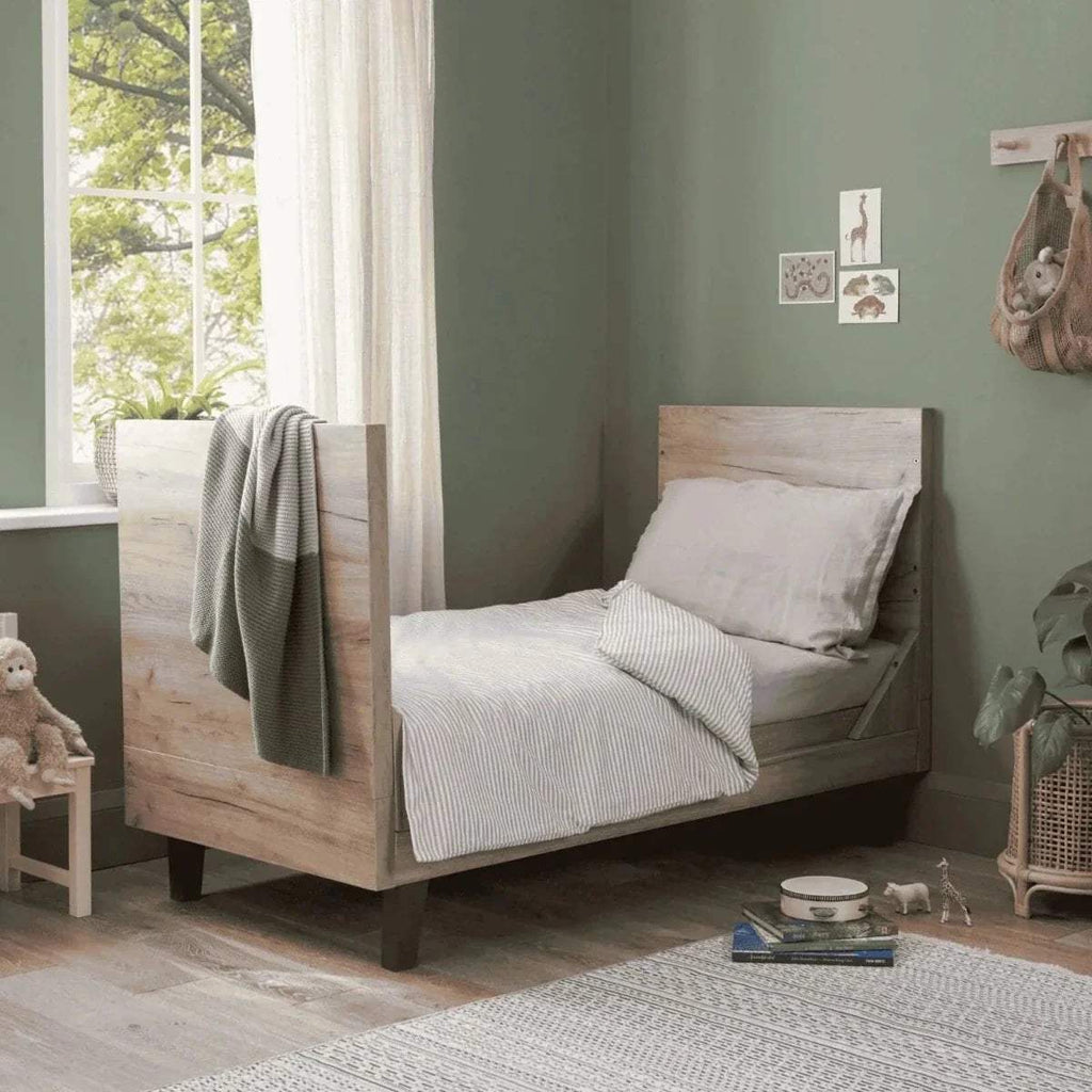 Distressed oak cot bed with white mattress, gray bedding, and slate grey slat sides