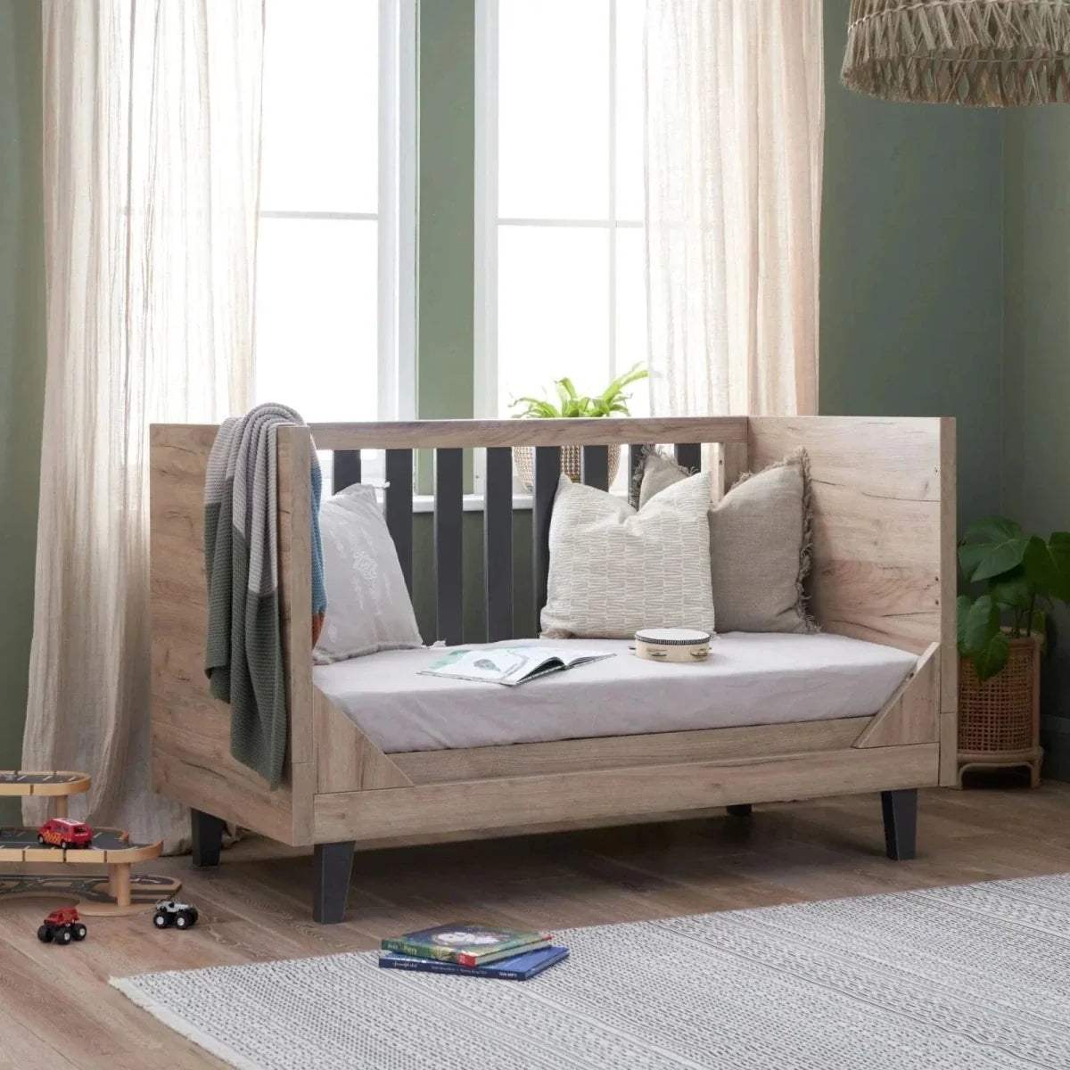 Distressed oak cot bed with white mattress and pillows, slate grey slat railing