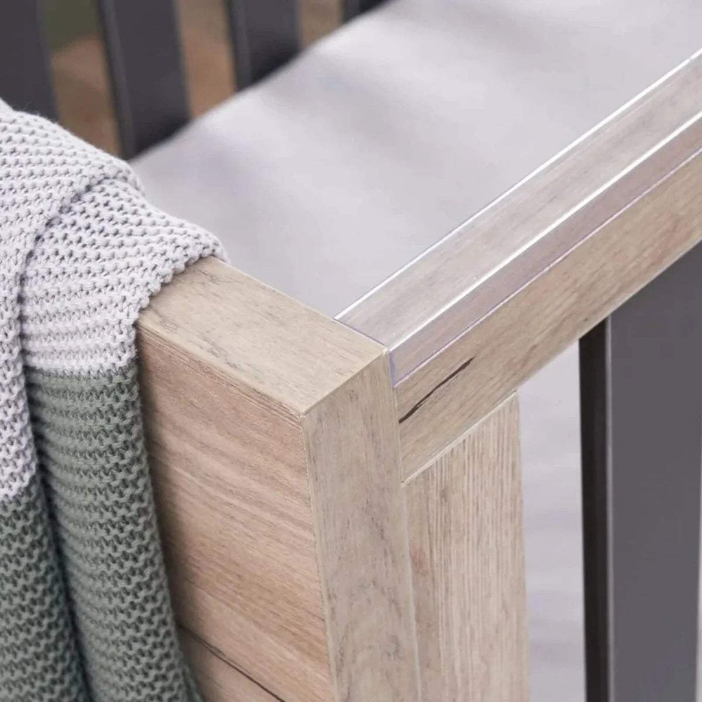 Close-up of distressed oak cot bed corner with slate grey slat frame