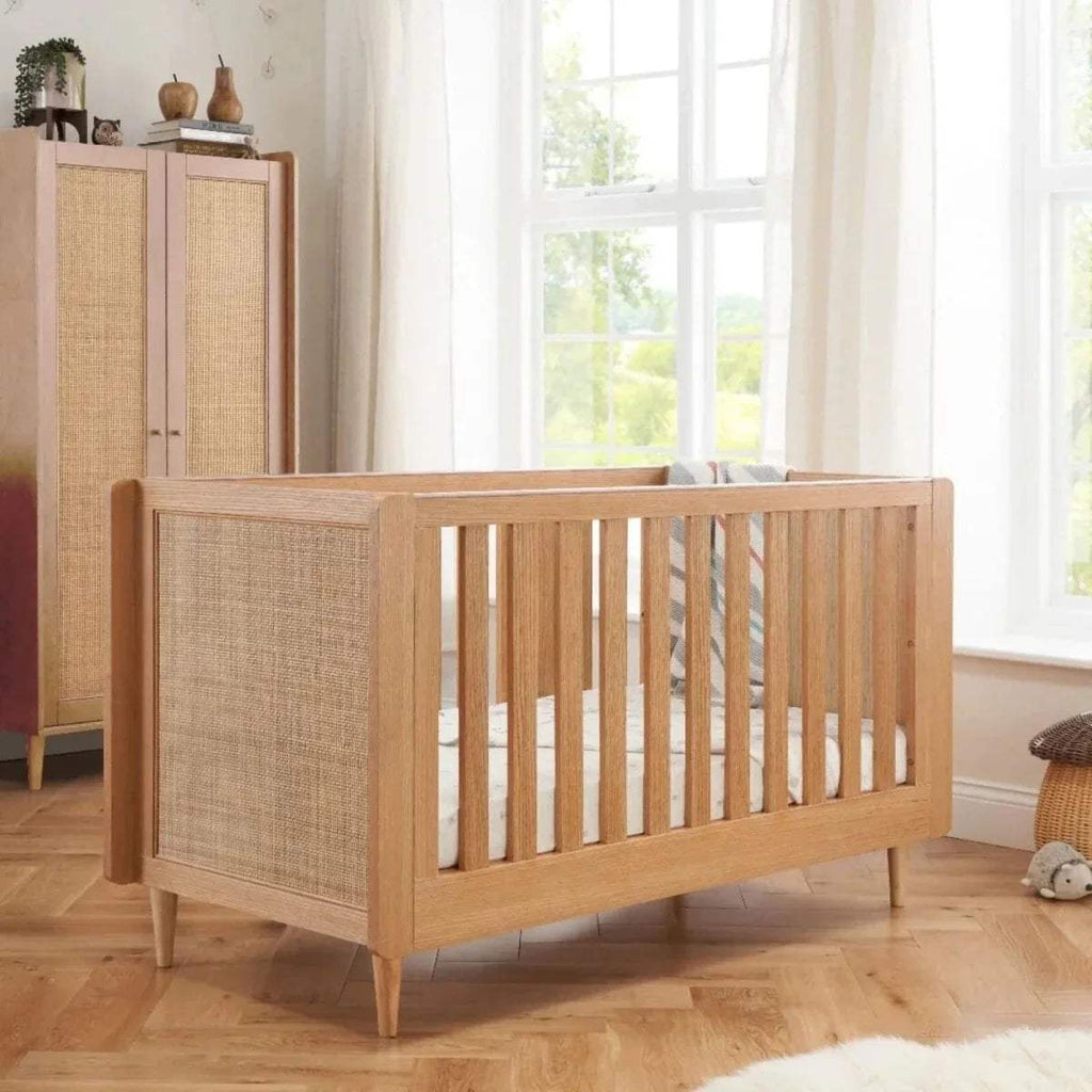 Light oak cot bed with vertical rail sides and woven fabric panels on headboard