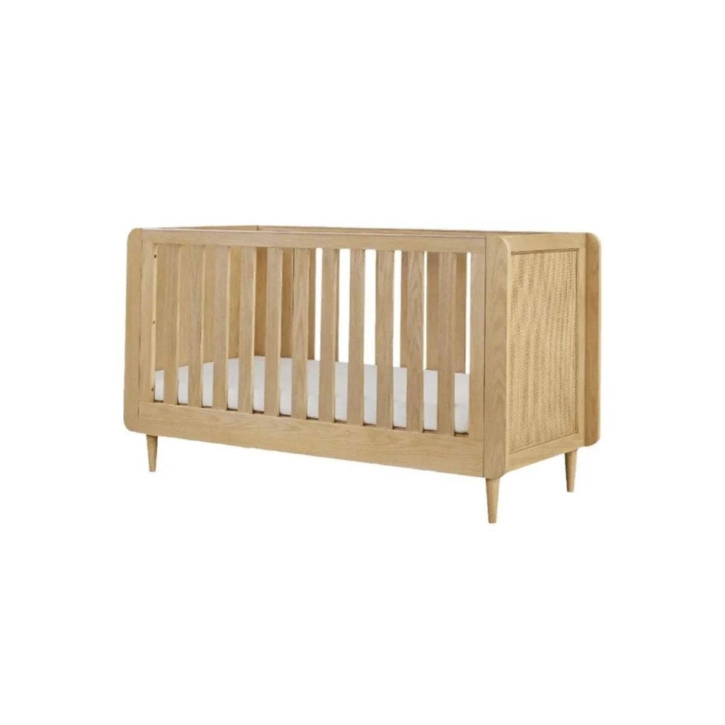 Light oak cot bed angled front view with vertical slat rails and woven side panels