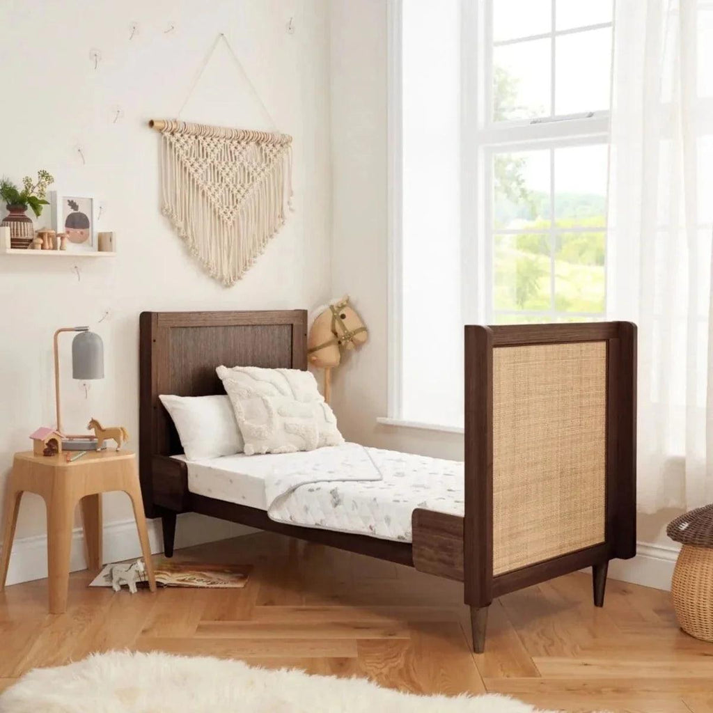 Warm walnut cot bed with woven end panel and vertical slat side rails