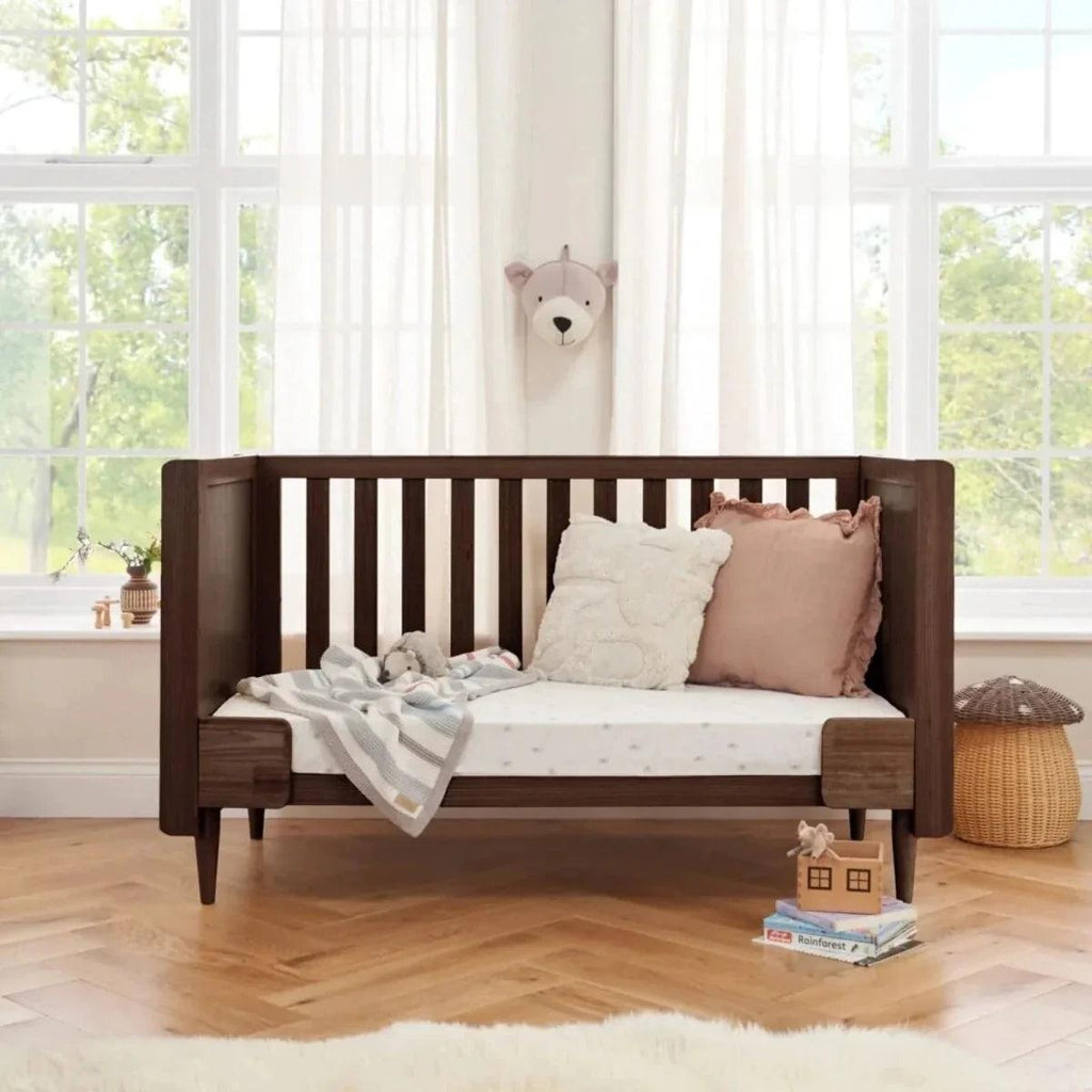 Warm walnut baby cot bed with vertical slat headboard and woven side panel