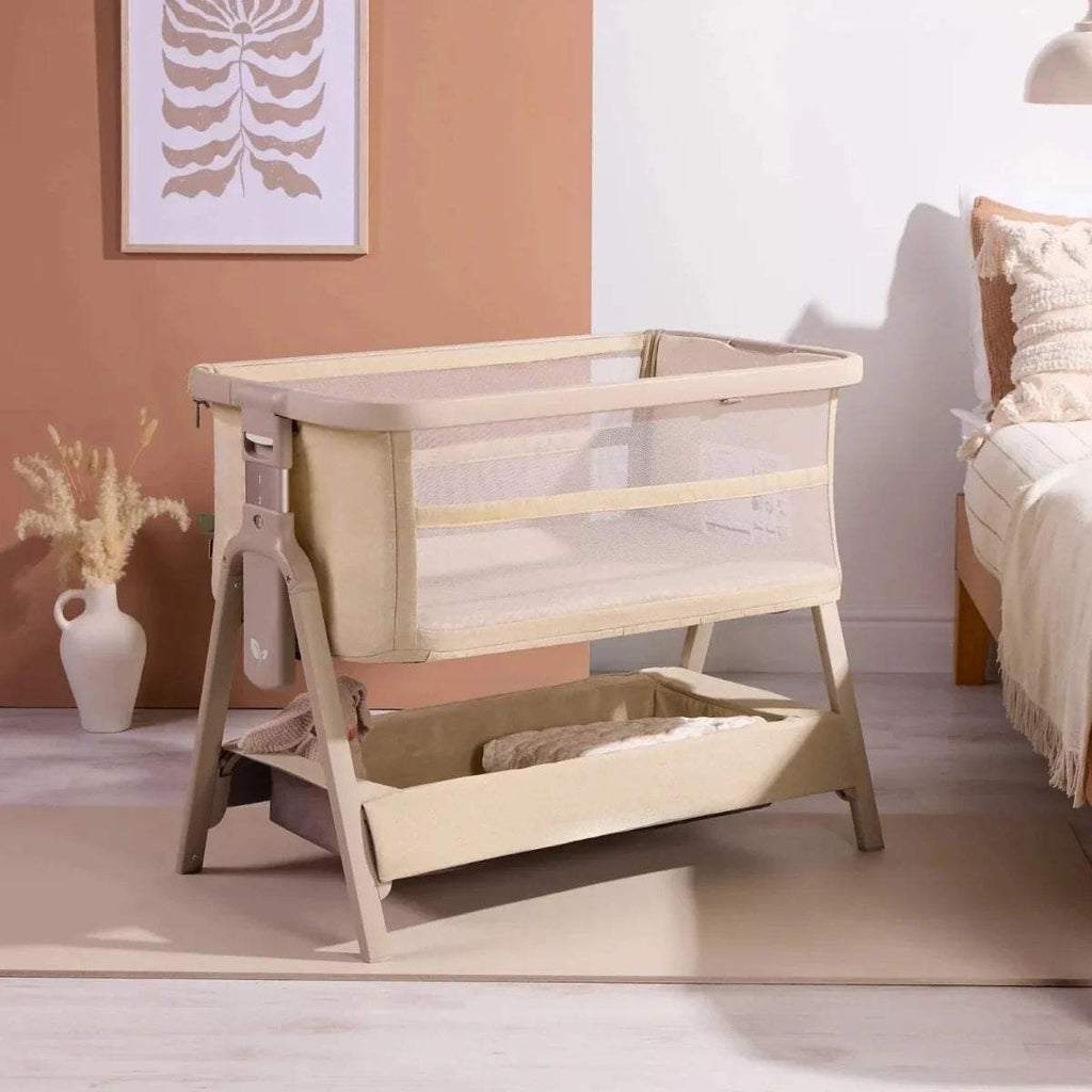 Sand bedside crib in a room, with open side rail and padded mattress base