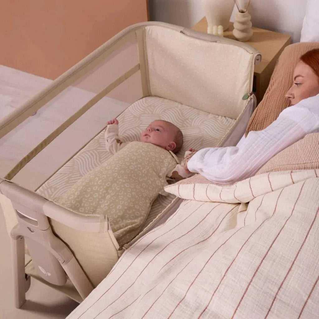 Sand bedside crib with baby resting on padded insert beside an adult