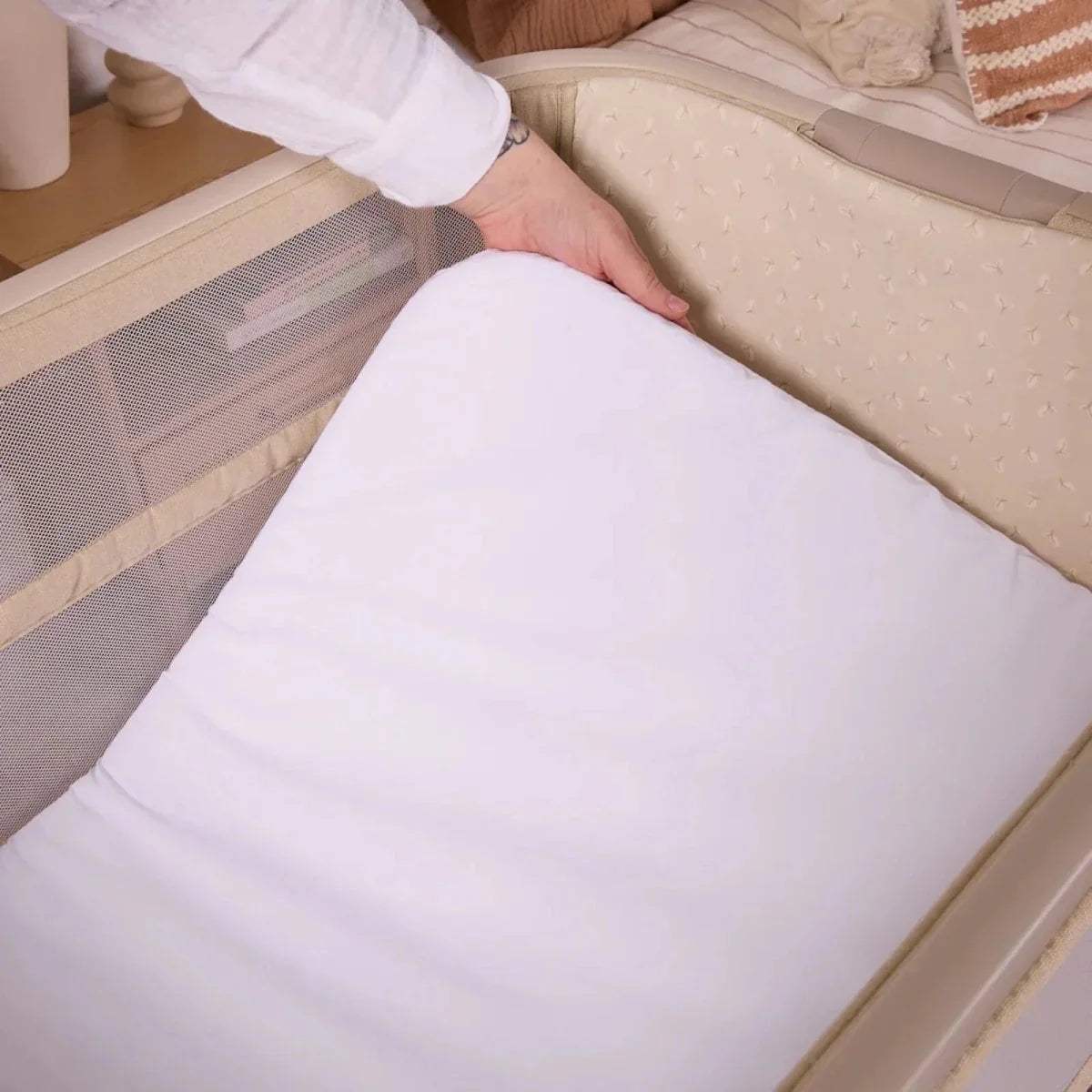 Sand bedside crib with white mattress pad and padded side walls