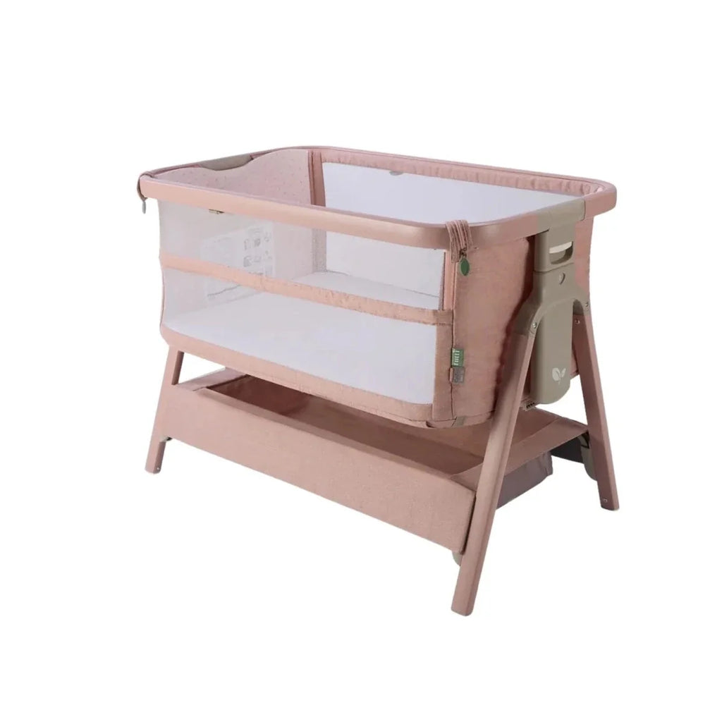 Blush bedside crib with mesh sides, padded base, and wooden support legs.
