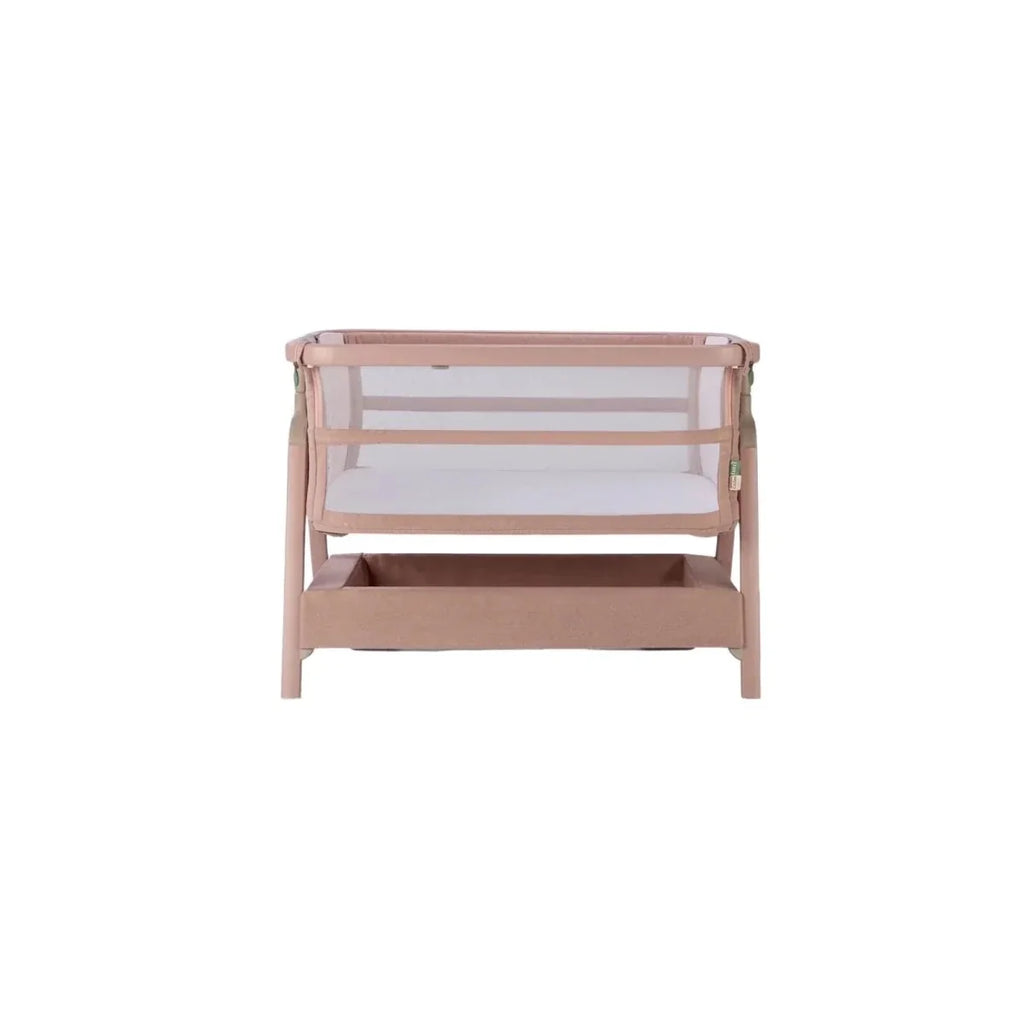 Blush bedside crib front view with mesh panel and padded mattress.