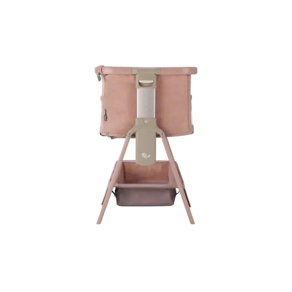 Blush bedside crib with front storage compartment and four wooden legs.