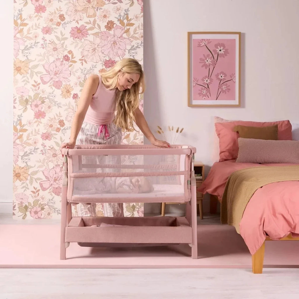 Blush bedside crib with mesh sides and lower storage drawer in a standing position.