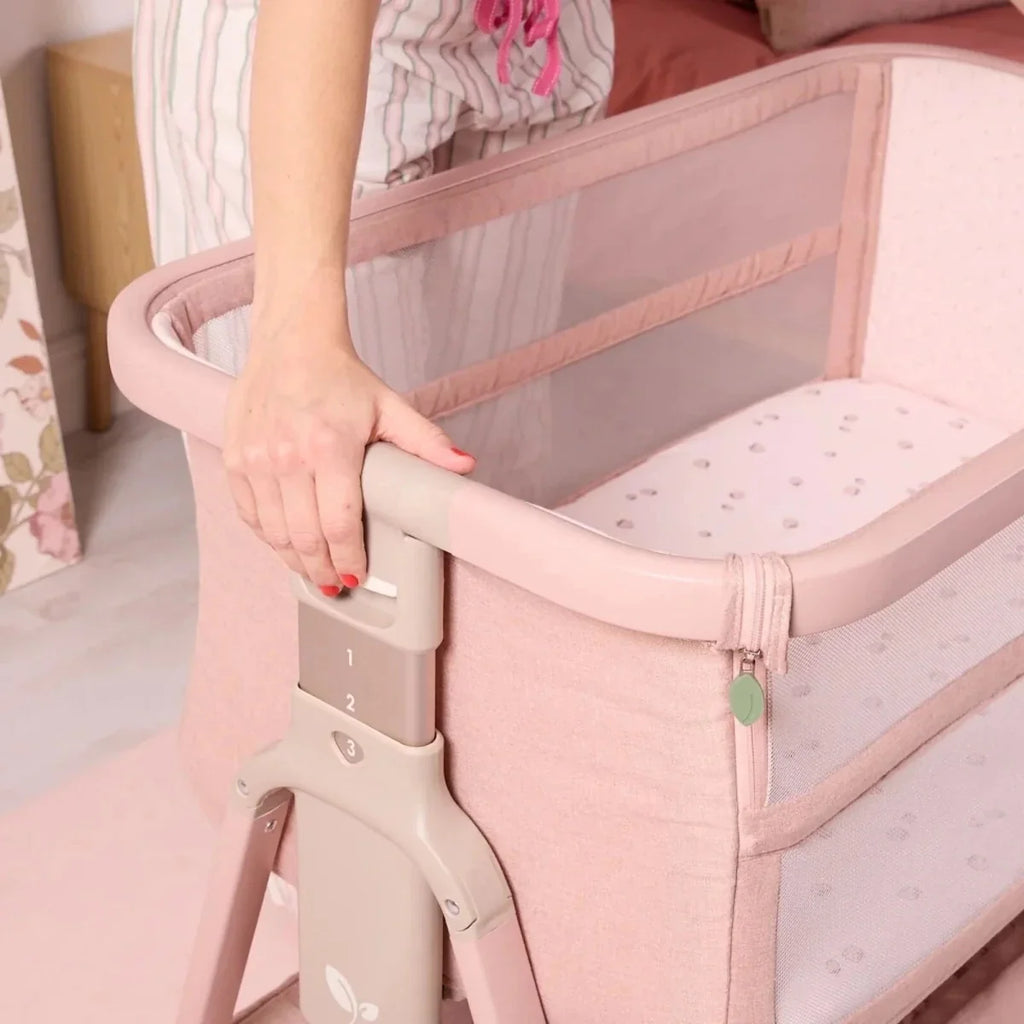 Blush pink bedside crib with open side and adjustable height legs