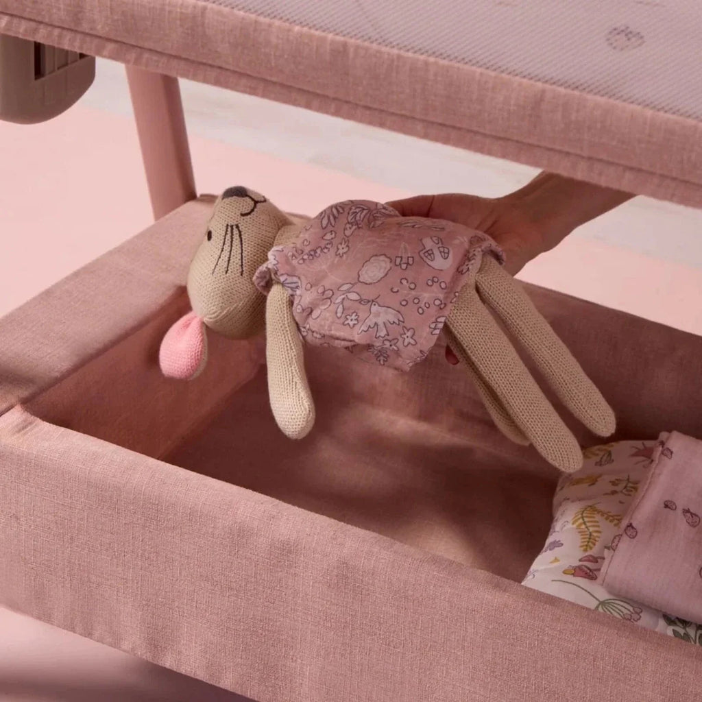 Blush bedside crib with padded interior, mesh side, and plush toy