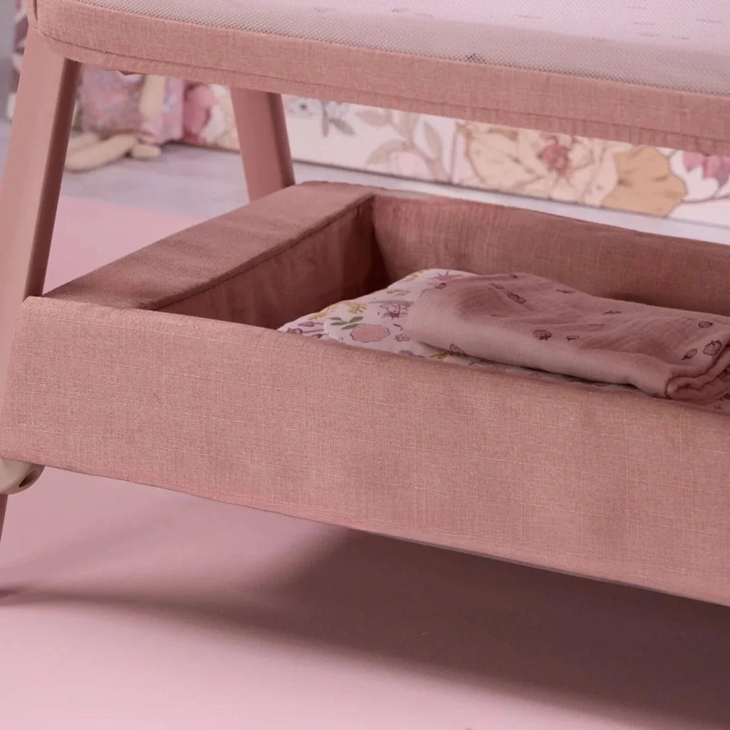 Blush bedside crib interior corner with cushioned rails and folded blanket