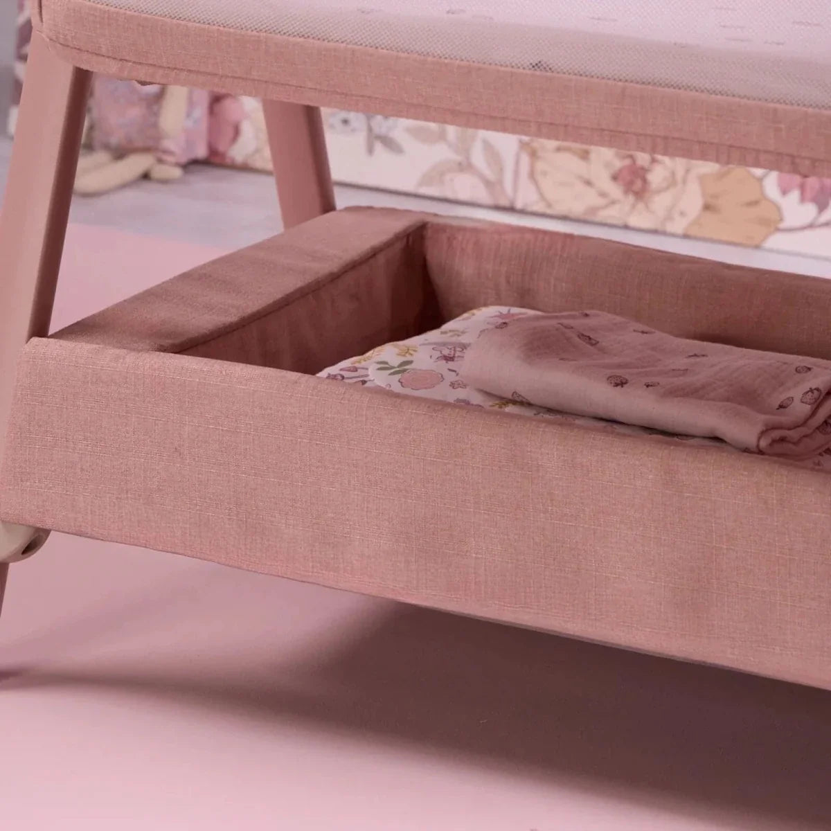 Blush bedside crib interior corner with cushioned rails and folded blanket