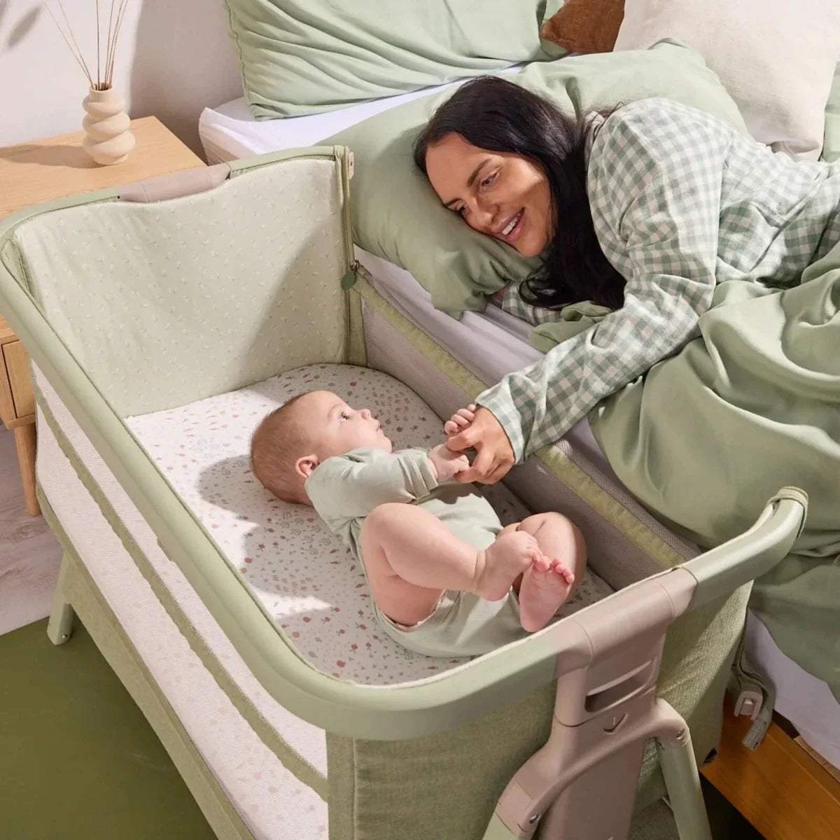 Eucalyptus green bedside crib with raised side rail, padded mattress, and open entry