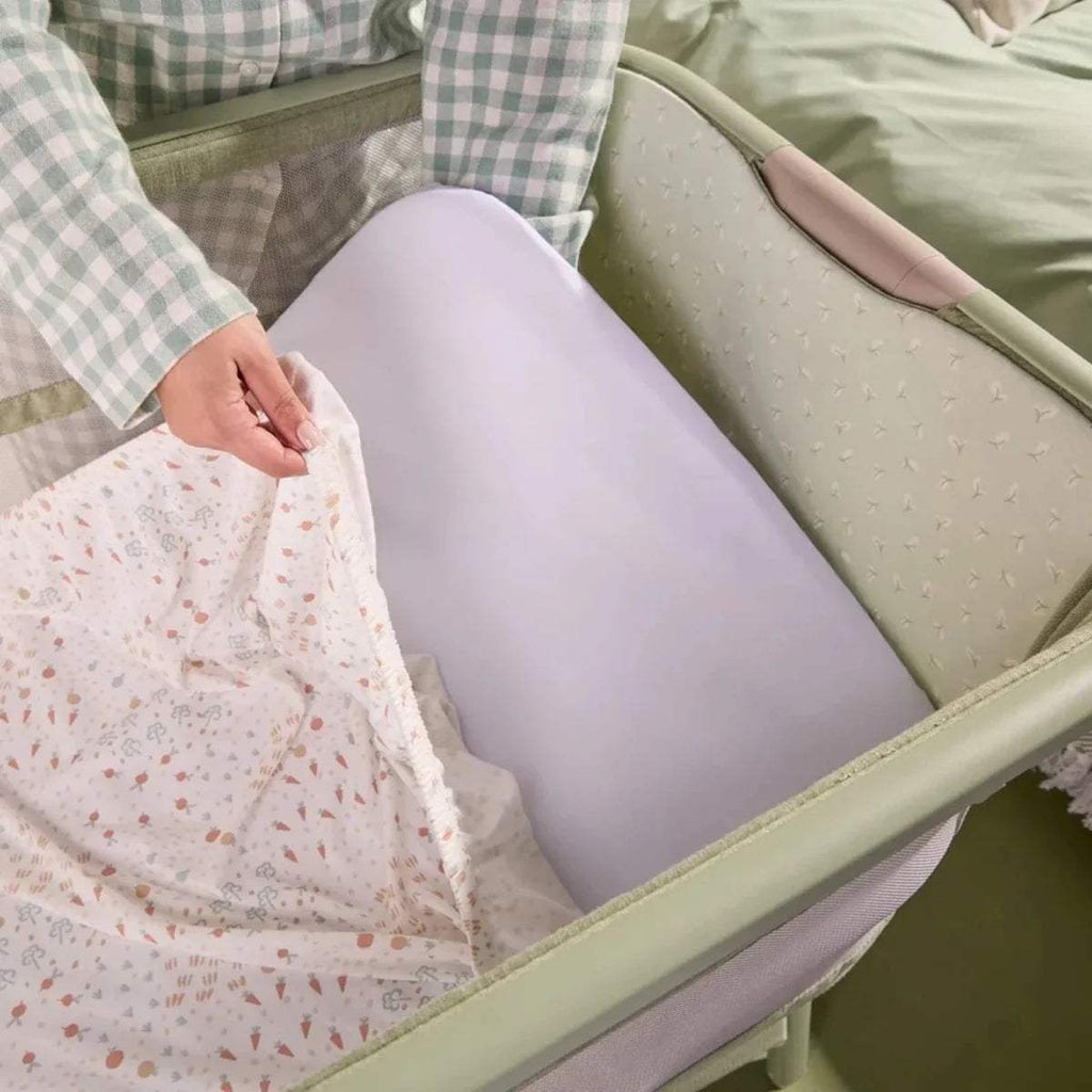 Eucalyptus bedside crib with open side showing pink patterned mattress pad