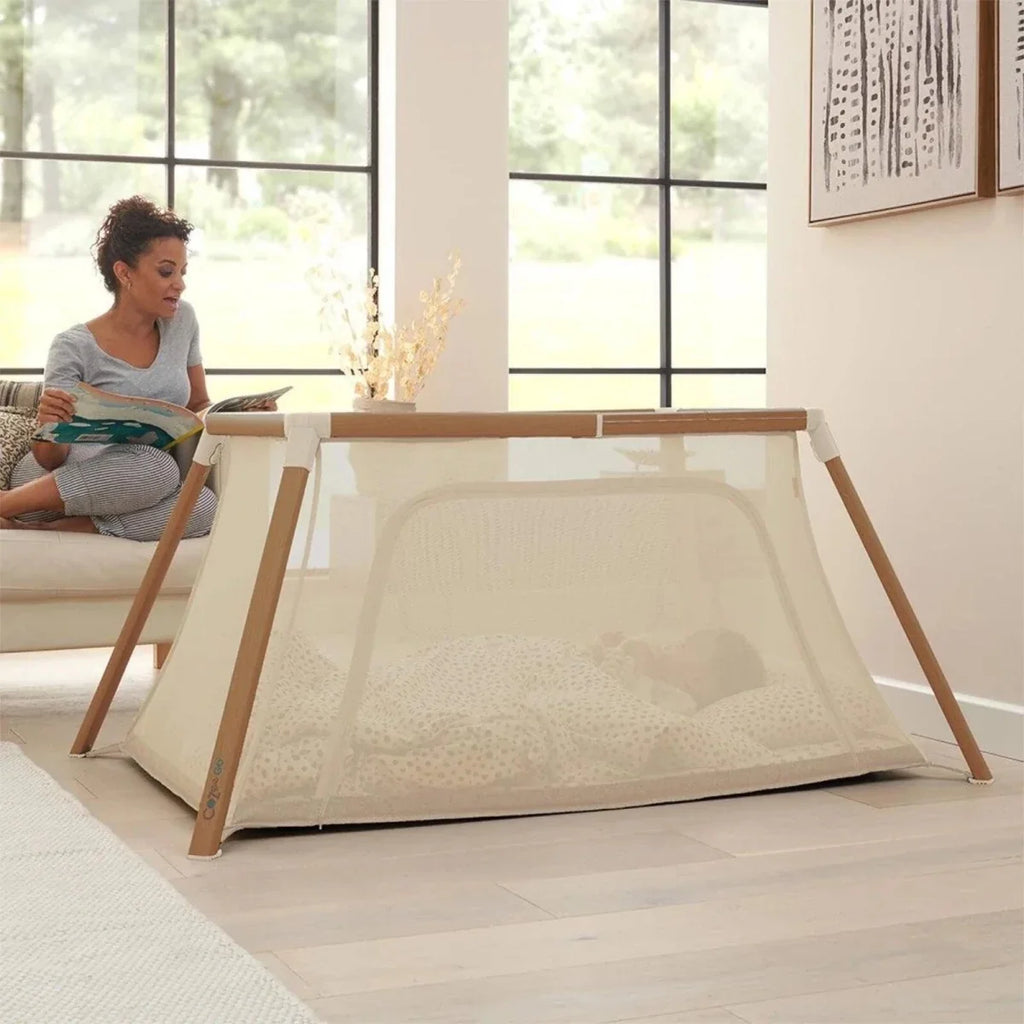 Baby playpen with ecru mesh panels and light wood frame, open side view