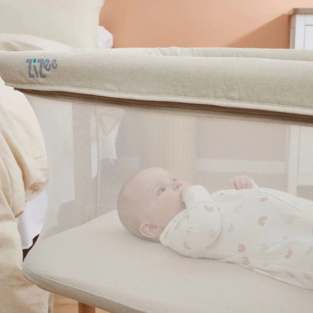 Ecru crib with mesh sides and baby lying on padded mattress