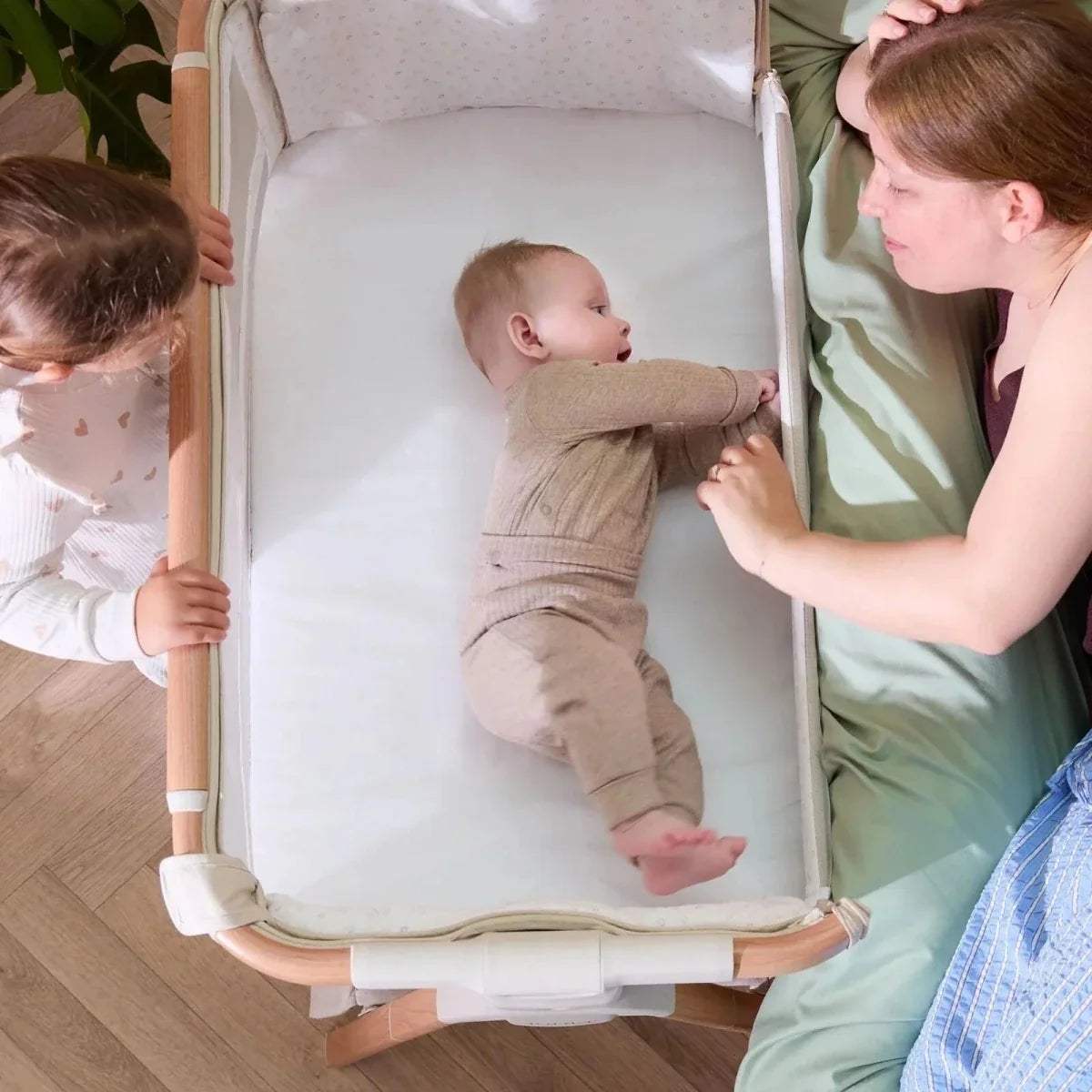 Walnut and ecru bedside crib with baby lying inside and open front rail
