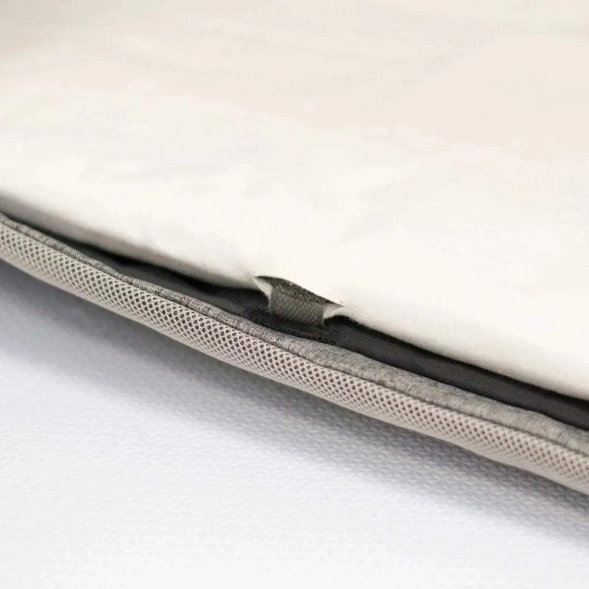 Close-up edge of white fitted sheet showing mesh layer and black seam line.