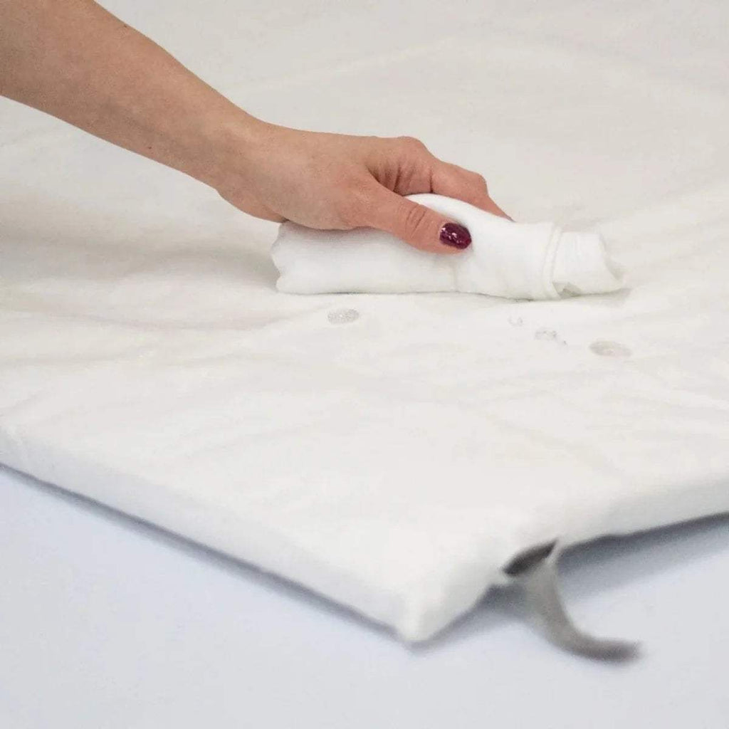 Hand smoothing a white fitted waterproof sheet corner, fitted creases visible.
