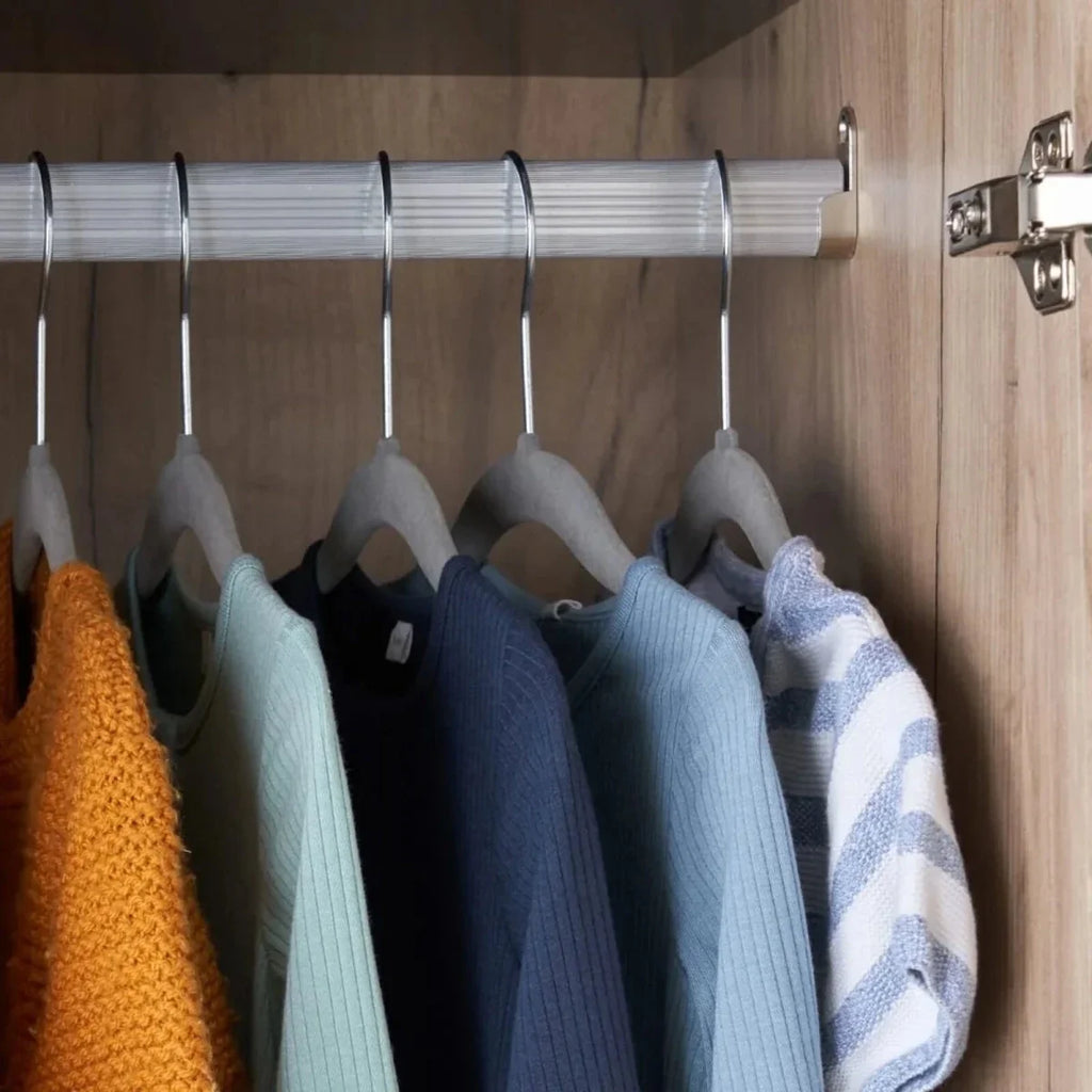 Wardrobe interior with hanging clothes on a metal rail, dark hooks and light wood wall.