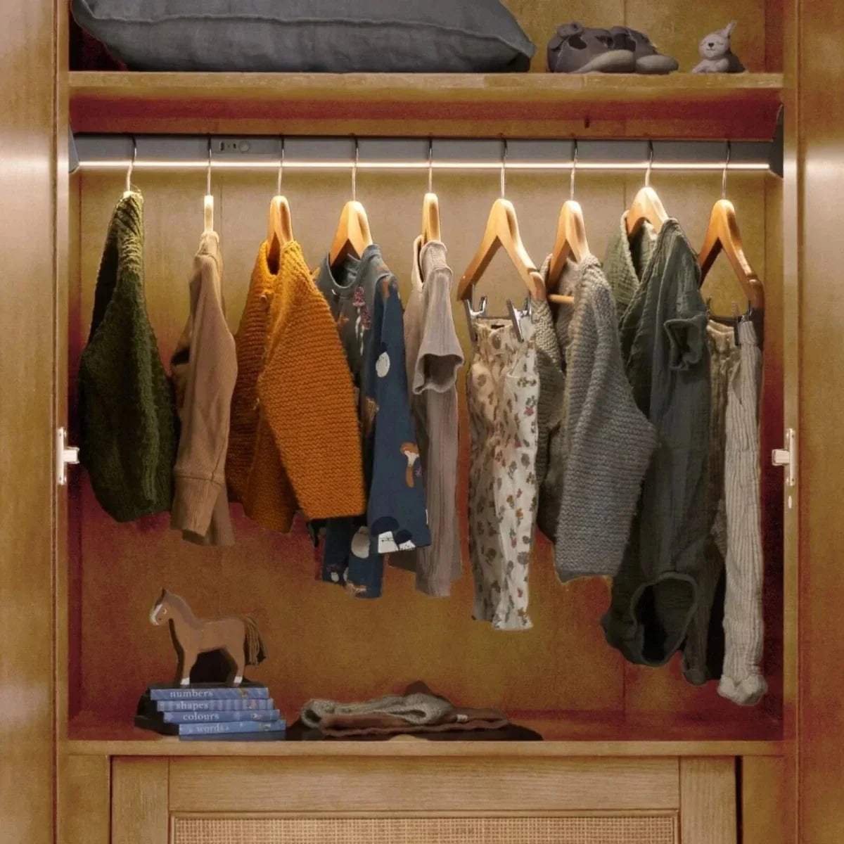 Open light oak wardrobe with hanging clothes on a central rail