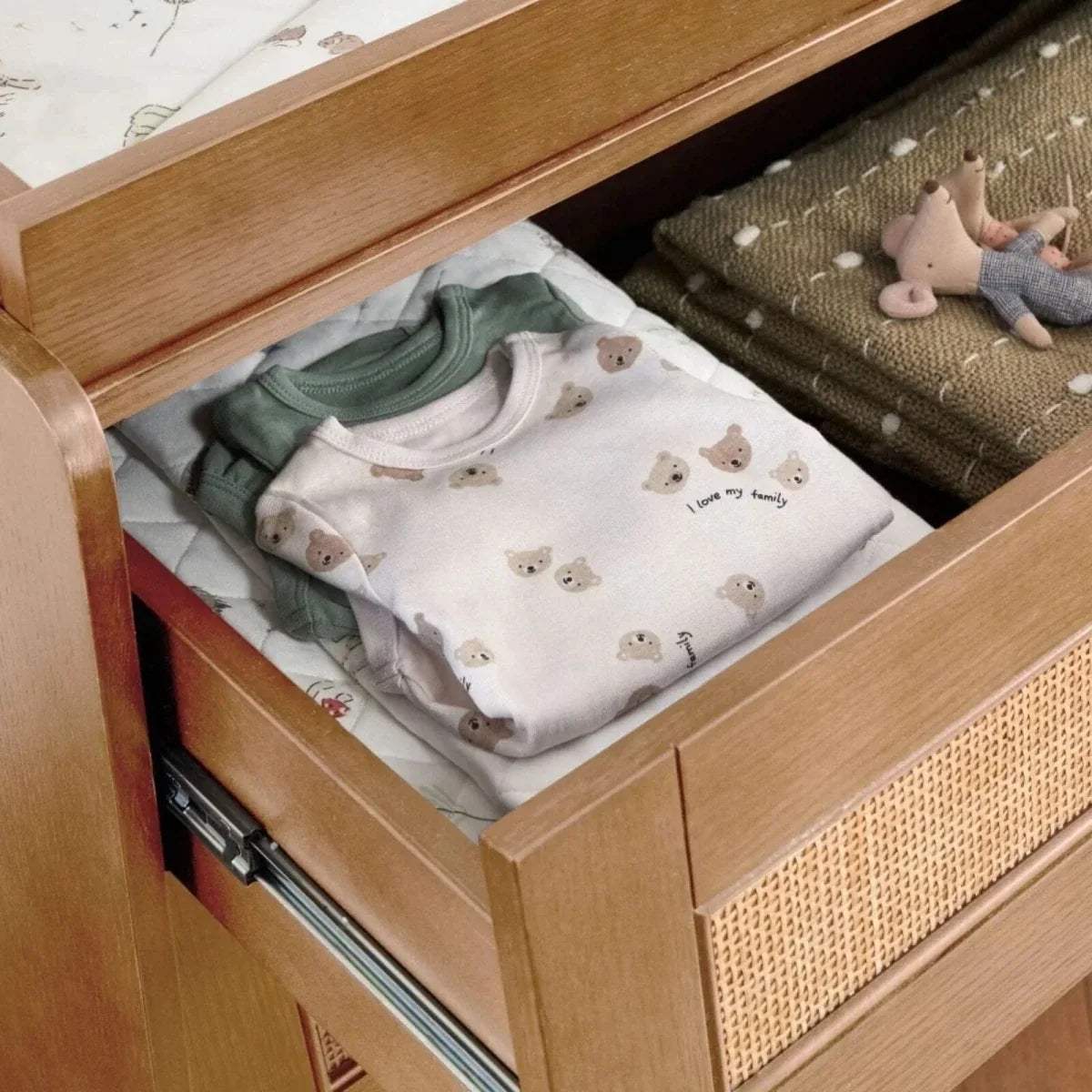 Light oak wardrobe drawer open with folded baby clothes and fabric divider