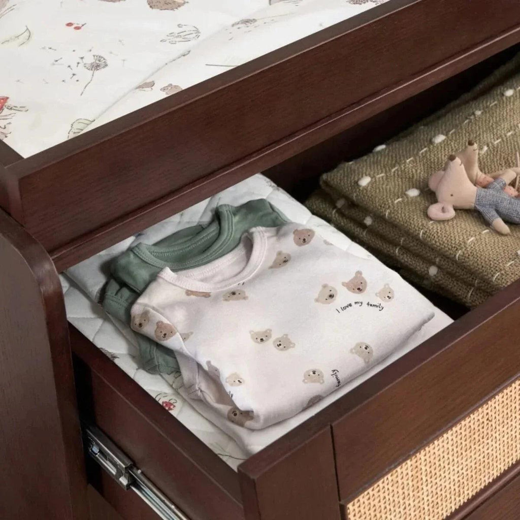 Open wardrobe drawer with neatly folded baby shirts on a woven inner panel