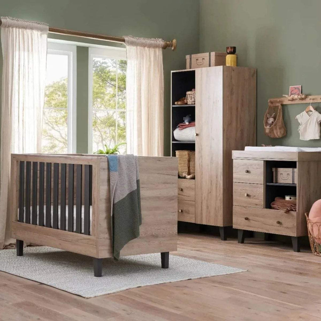 Baby changing chest in light wood with open shelf, shown from side angle in a room