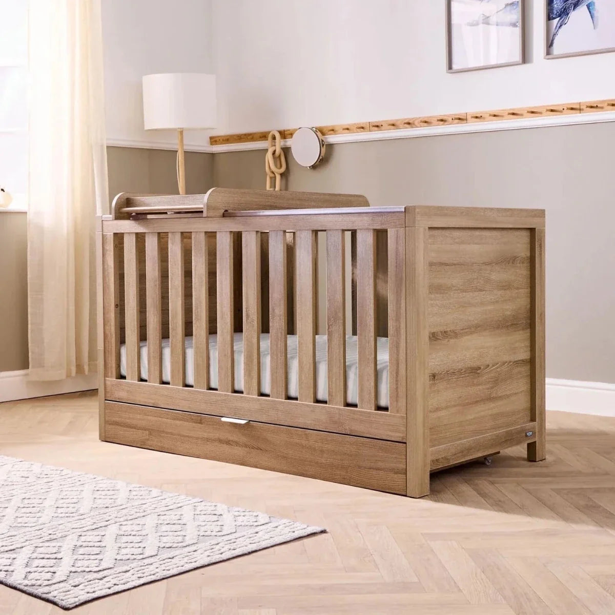 Light wood underbed drawer attached below crib frame with pull-out front