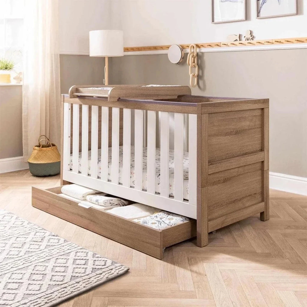 Oak underbed drawer installed beneath crib, open with pull handle