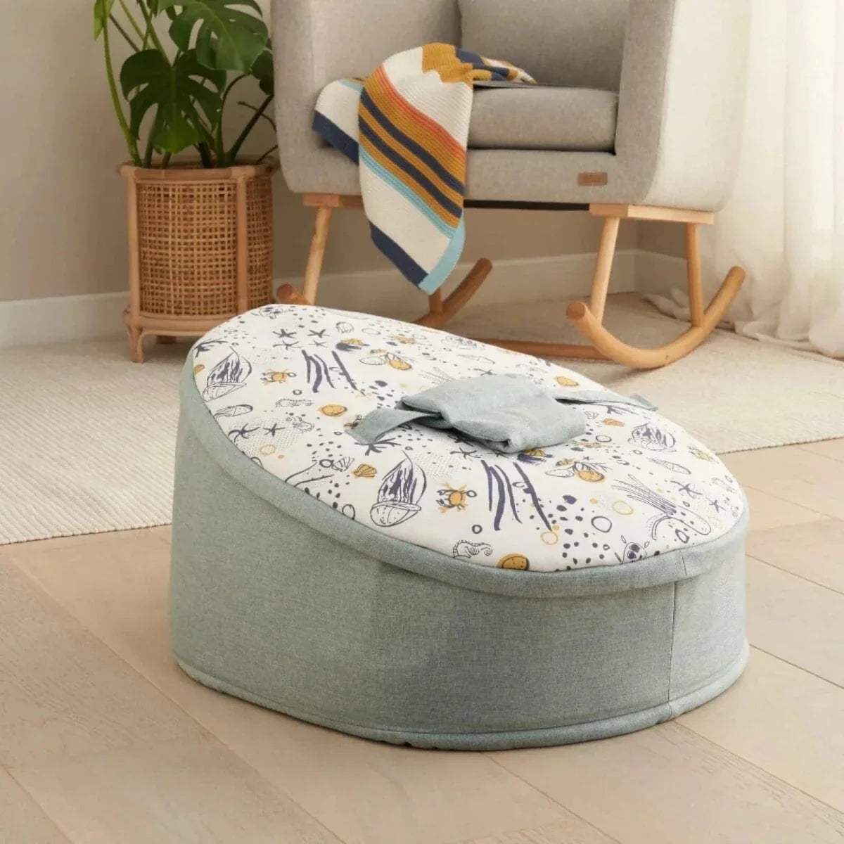 Baby beanbag with pale blue cover and ocean-themed print, rounded design with carrying handle.