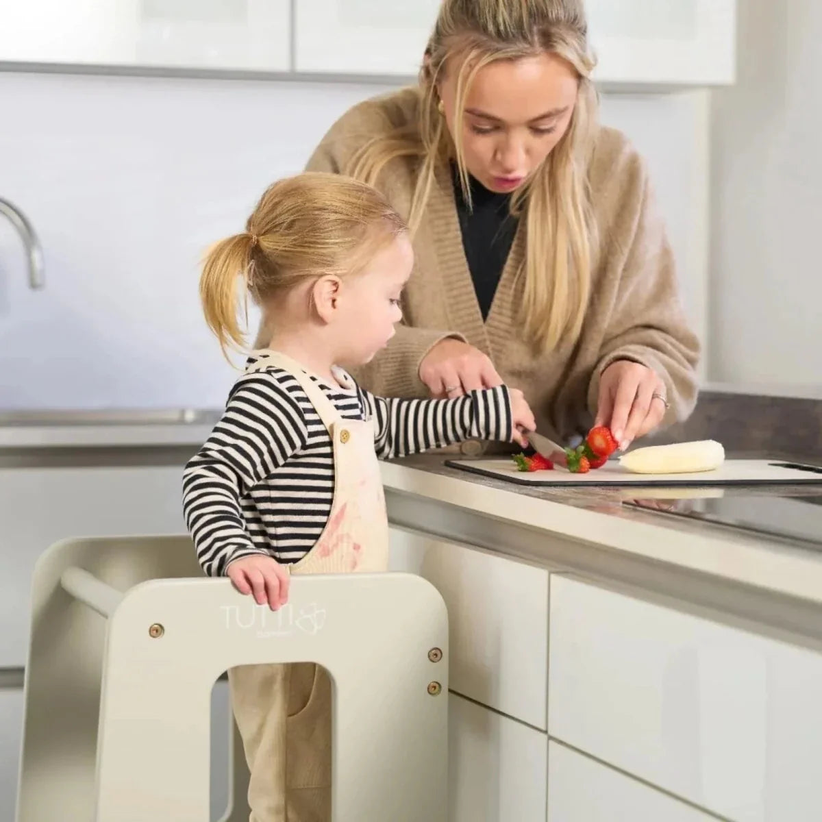 Light beige toddler learning tower with small child standing and cooking at counter