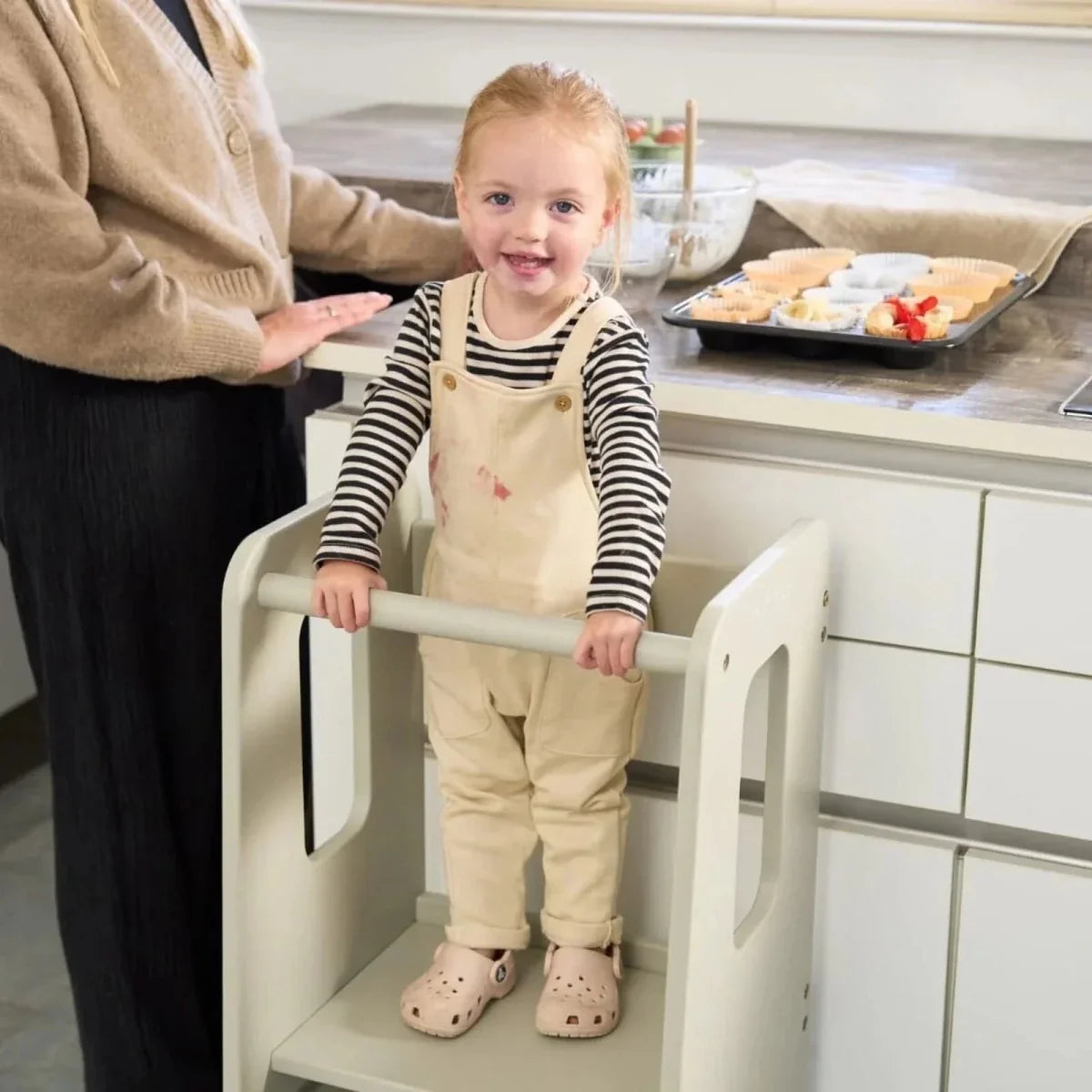 Light beige toddler learning tower with child standing on top step holding rail