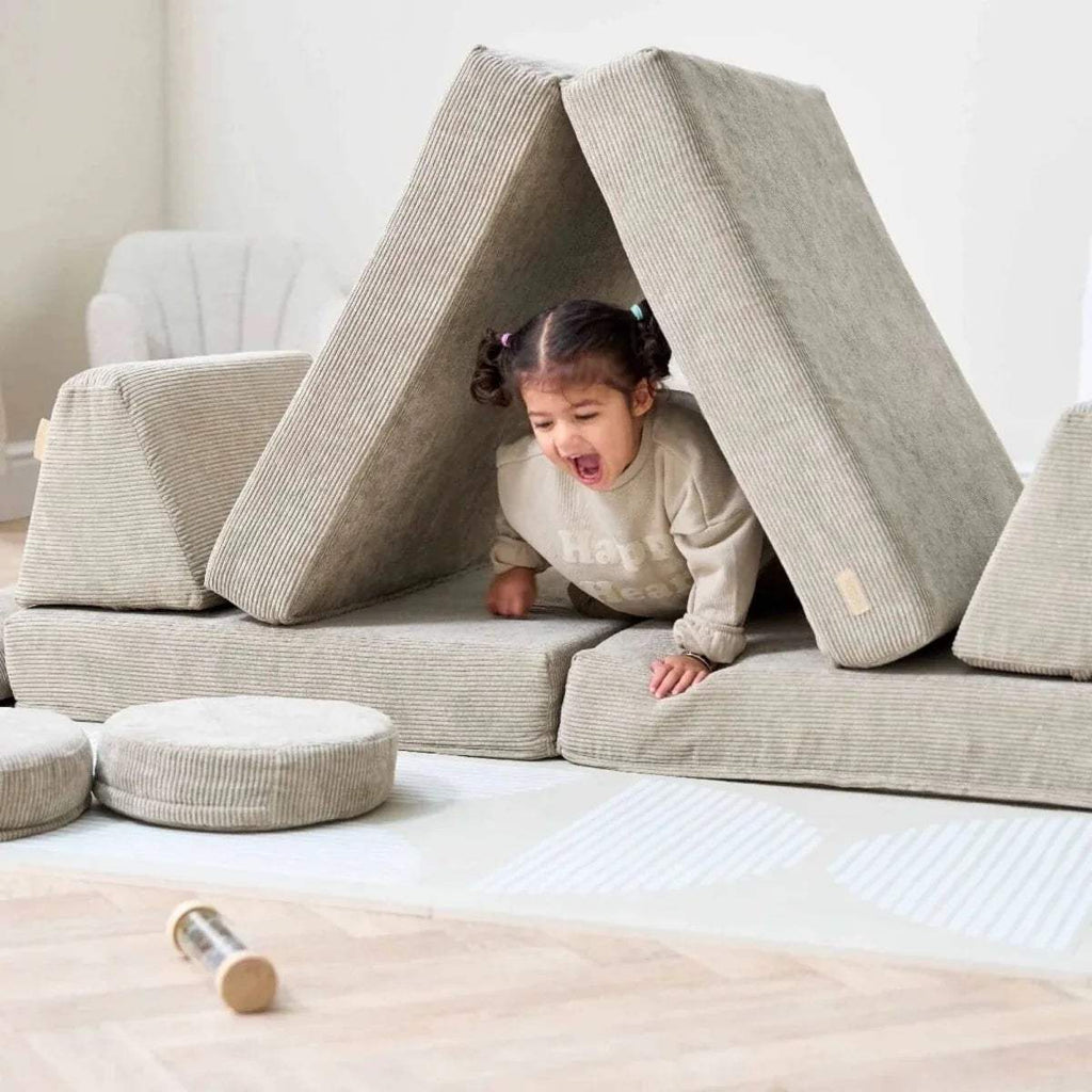Child playing on mushroom-beige play sofa with freestanding triangular cushion panels